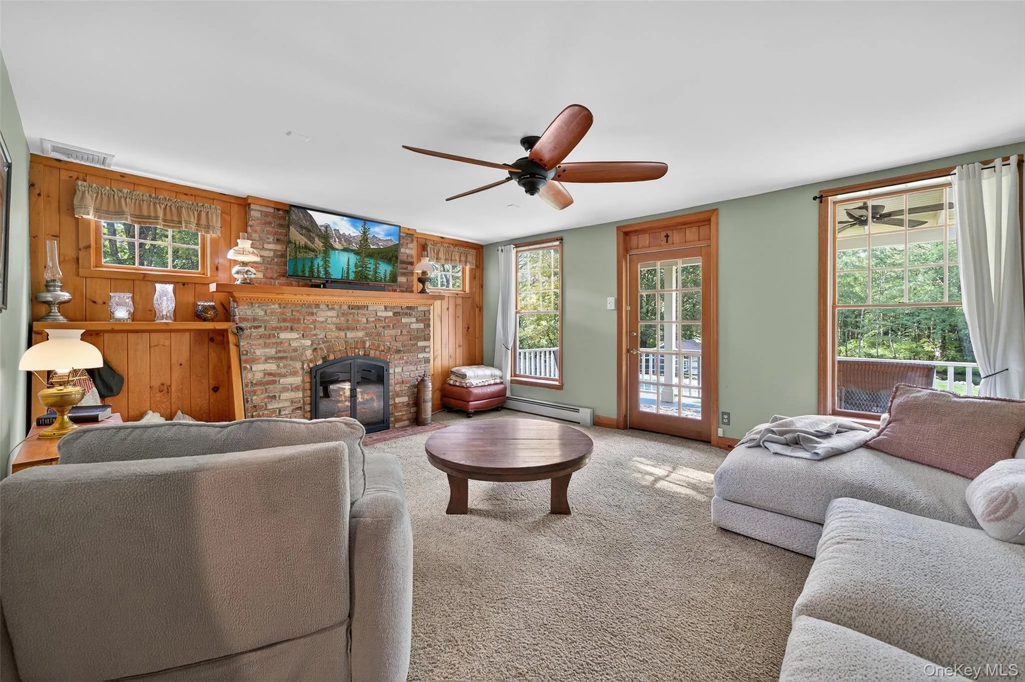 Living area with carpet flooring, wood walls, a baseboard heating unit, a ceiling fan, and a fireplace Living area with carpet flooring, wood walls, a baseboard heating unit, a ceiling fan, and a fireplace