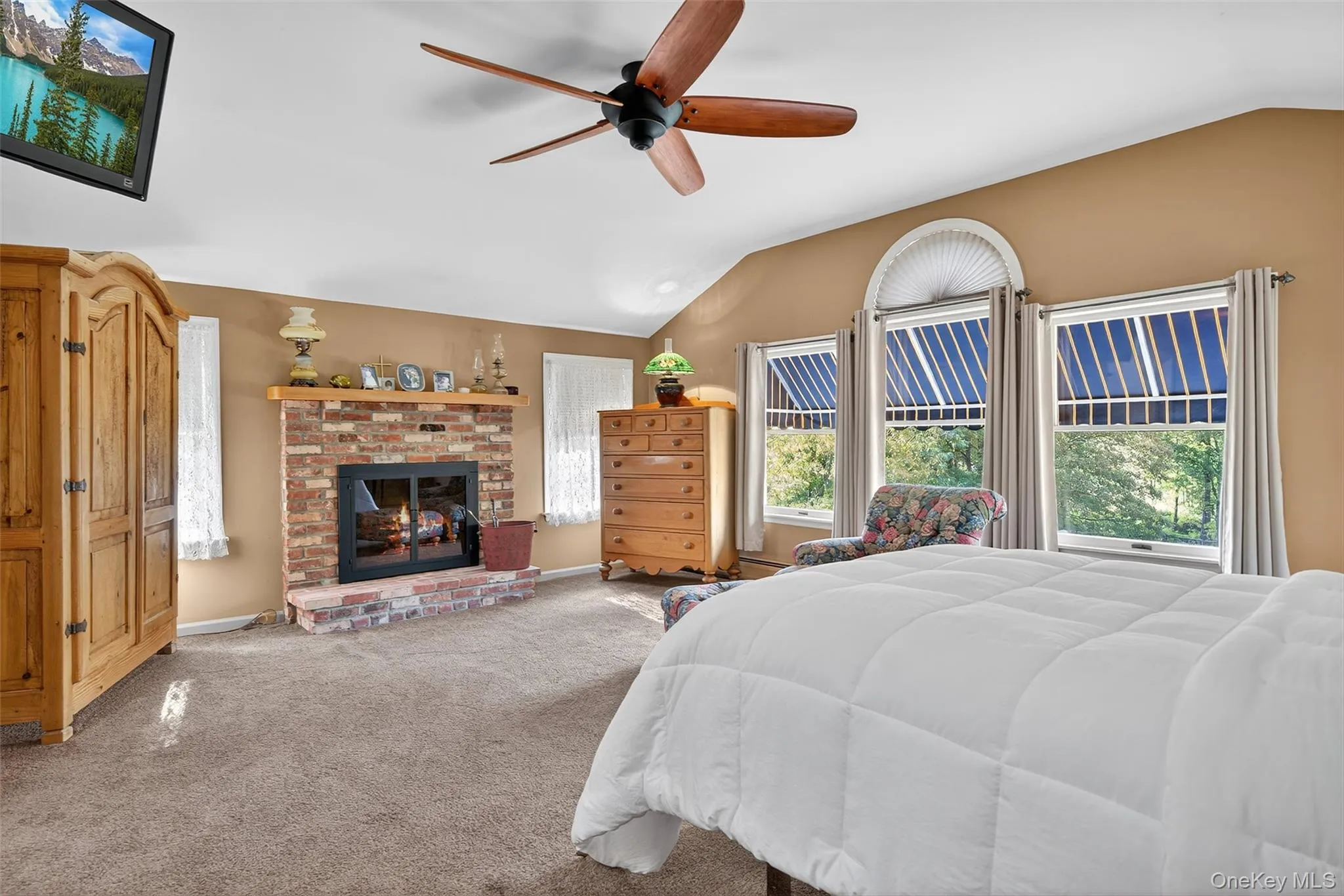 Carpeted bedroom featuring lofted ceiling, a fireplace, and a ceiling fan Carpeted bedroom featuring lofted ceiling, a fireplace, and a ceiling fan