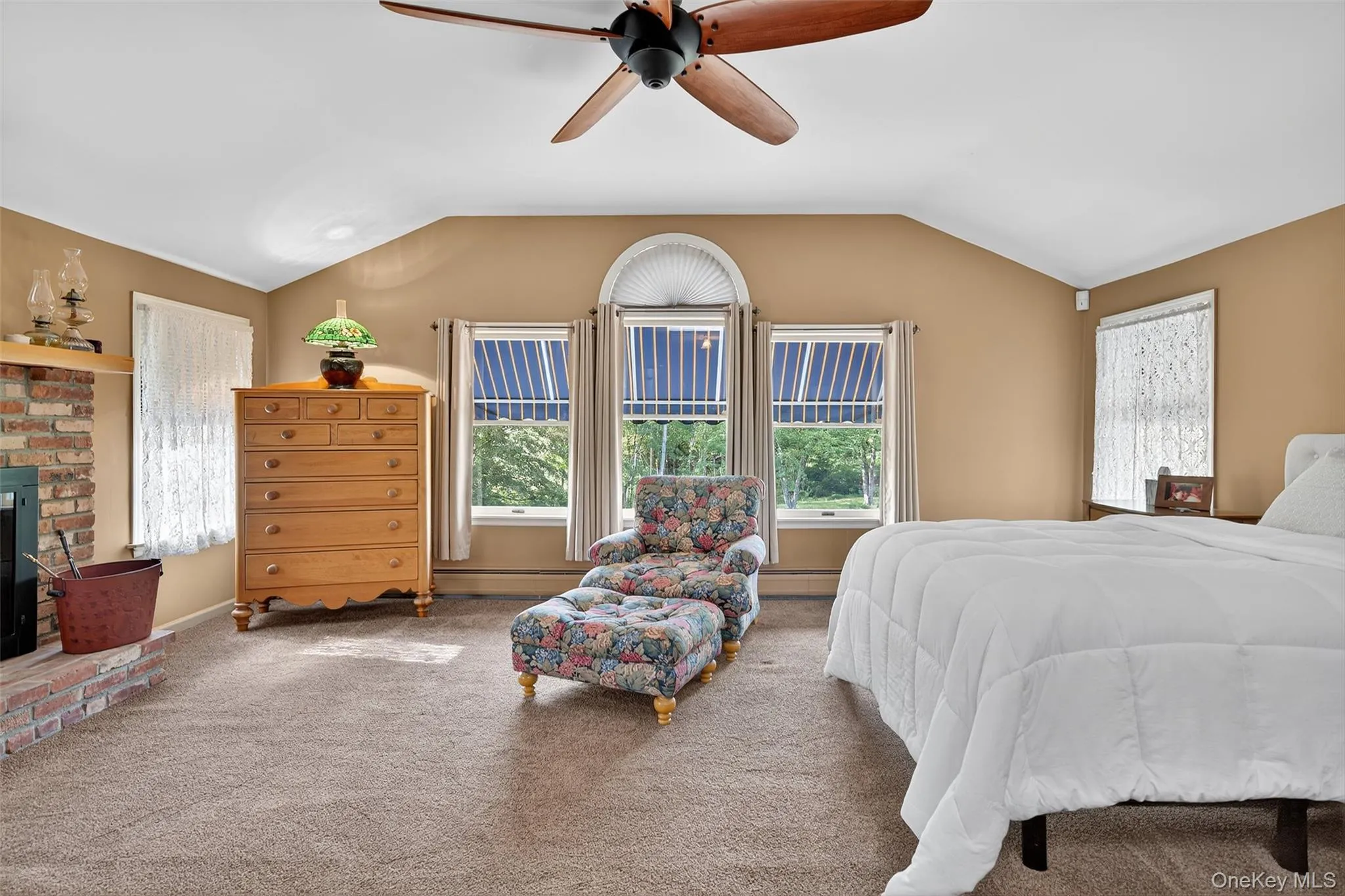 Bedroom with carpet floors, multiple windows, lofted ceiling, a fireplace, and ceiling fan Bedroom with carpet floors, multiple windows, lofted ceiling, a fireplace, and ceiling fan