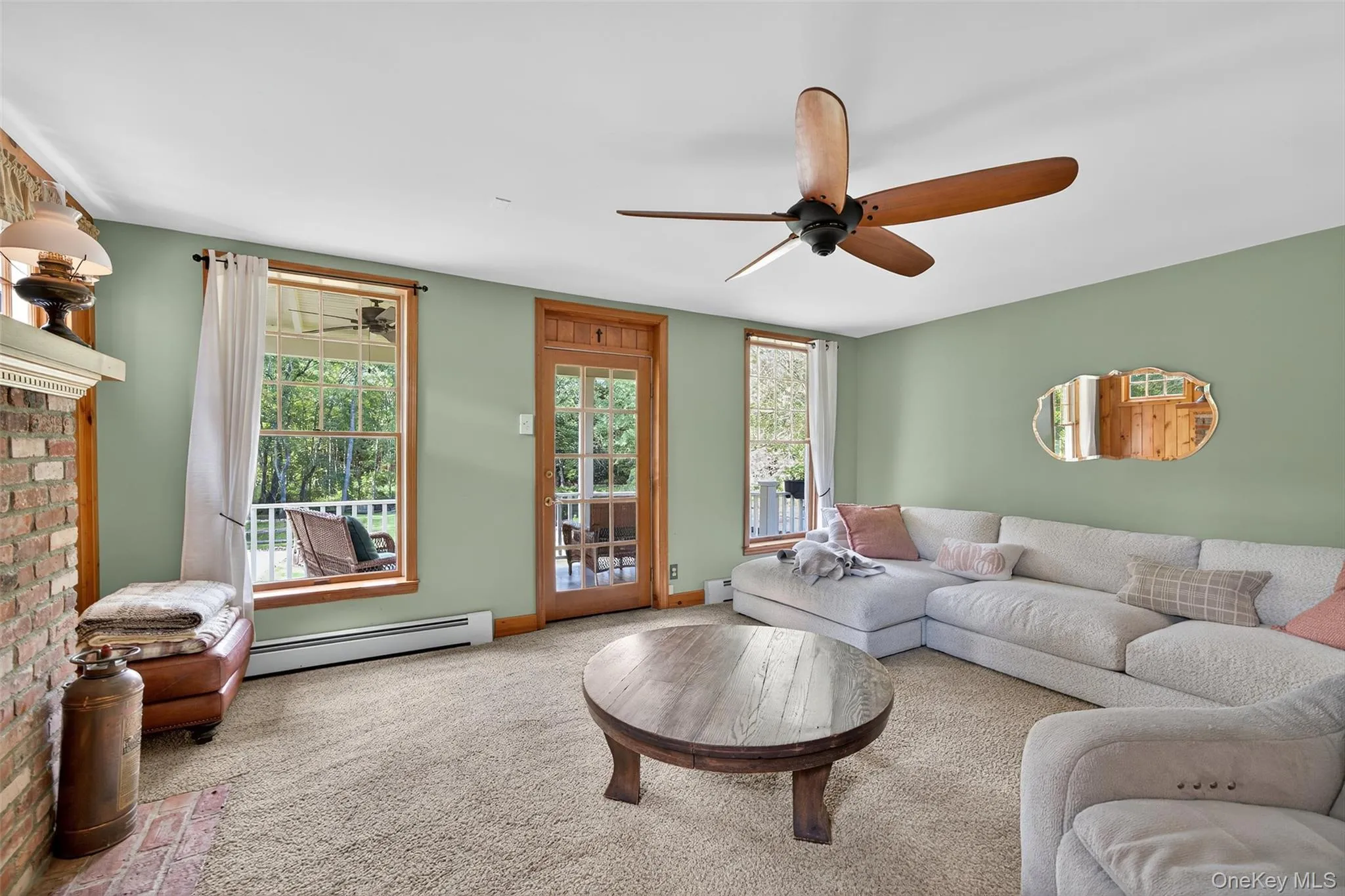 Carpeted living area featuring a baseboard radiator, plenty of natural light, a ceiling fan, and a fireplace Carpeted living area featuring a baseboard radiator, plenty of natural light, a ceiling fan, and a fireplace