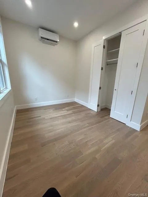 Unfurnished bedroom with light wood finished floors, a closet, recessed lighting, and an AC wall unit Unfurnished bedroom with light wood finished floors, a closet, recessed lighting, and an AC wall unit