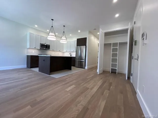 Kitchen featuring open floor plan, white cabinetry, pendant lighting, dark brown cabinetry, and stainless steel appliances Kitchen featuring open floor plan, white cabinetry, pendant lighting, dark brown cabinetry, and stainless steel appliances