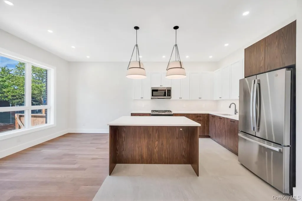 Kitchen featuring white cabinets, appliances with stainless steel finishes, hanging light fixtures, dark brown cabinetry, and a kitchen island Kitchen featuring white cabinets, appliances with stainless steel finishes, hanging light fixtures, dark brown cabinetry, and a kitchen island