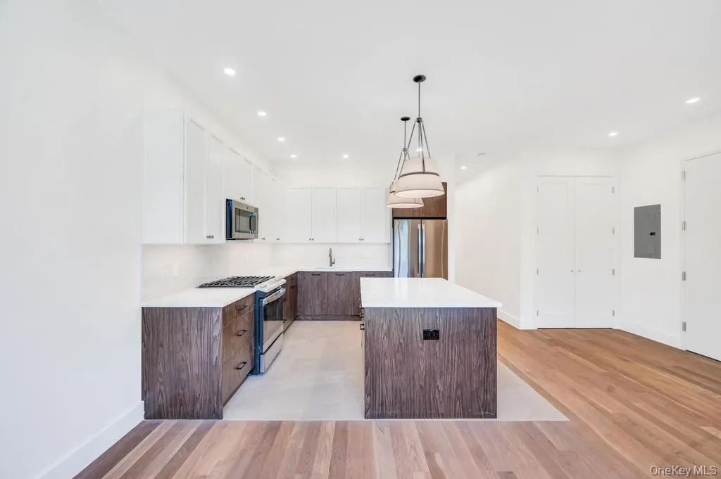 Kitchen featuring white cabinets, appliances with stainless steel finishes, pendant lighting, a kitchen island, and light wood-style floors Kitchen featuring white cabinets, appliances with stainless steel finishes, pendant lighting, a kitchen island, and light wood-style floors