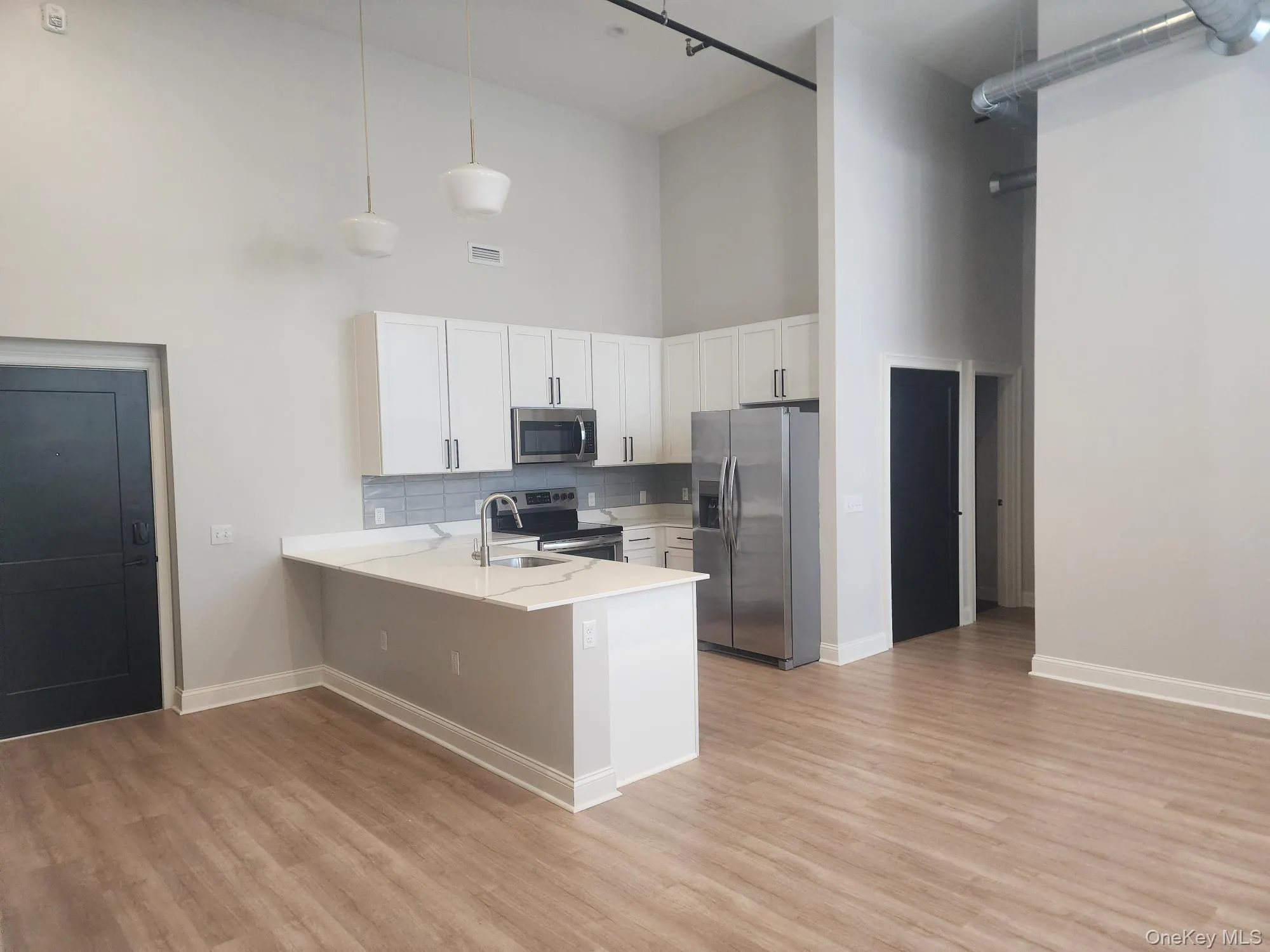 Kitchen featuring stainless steel appliances, a towering ceiling, a peninsula, white cabinets, and backsplash Kitchen featuring stainless steel appliances, a towering ceiling, a peninsula, white cabinets, and backsplash
