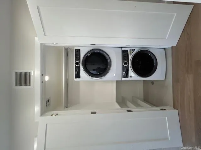 Washroom with stacked washer and clothes dryer and light wood finished floors Washroom with stacked washer and clothes dryer and light wood finished floors