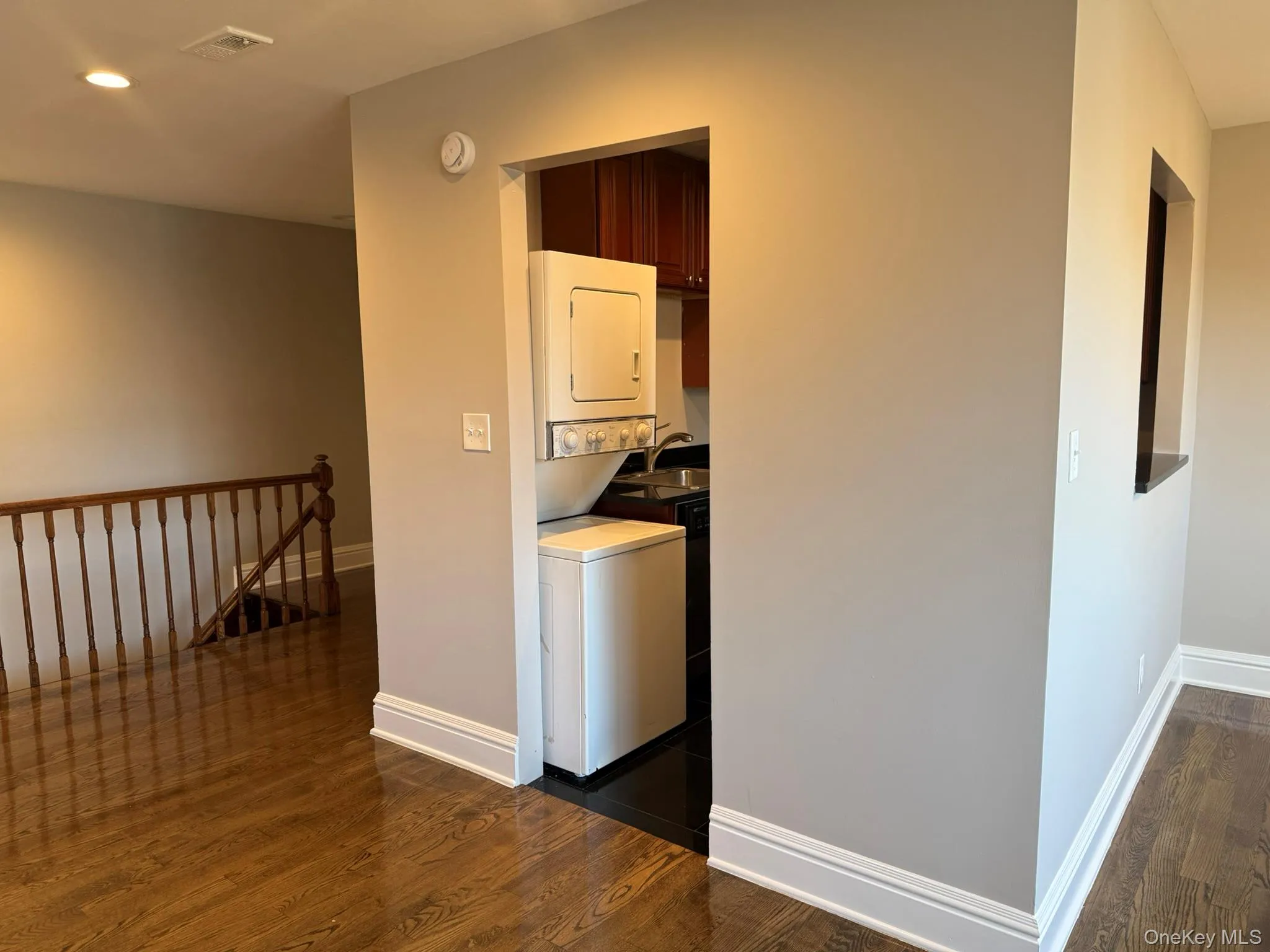 Laundry room featuring dark wood-type flooring, stacked washer and clothes dryer, and recessed lighting Laundry room featuring dark wood-type flooring, stacked washer and clothes dryer, and recessed lighting