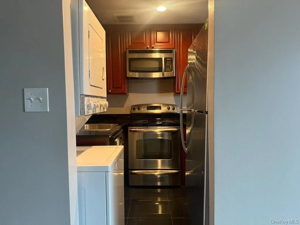 Kitchen featuring stainless steel appliances, tile counters, and dark tile patterned floors Kitchen featuring stainless steel appliances, tile counters, and dark tile patterned floors