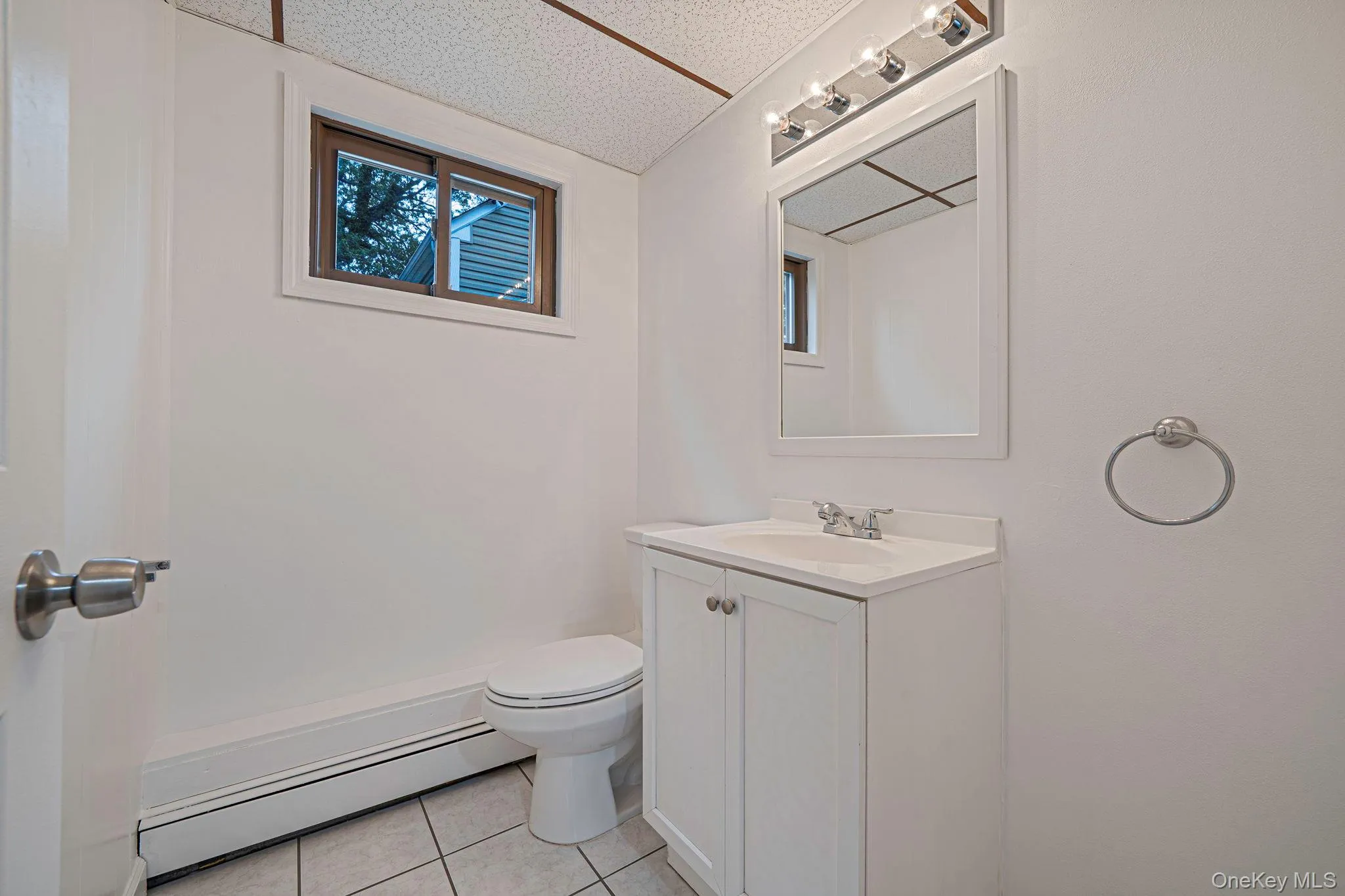 Half bath featuring vanity, light tile patterned floors, and a baseboard heating unit Half bath featuring vanity, light tile patterned floors, and a baseboard heating unit