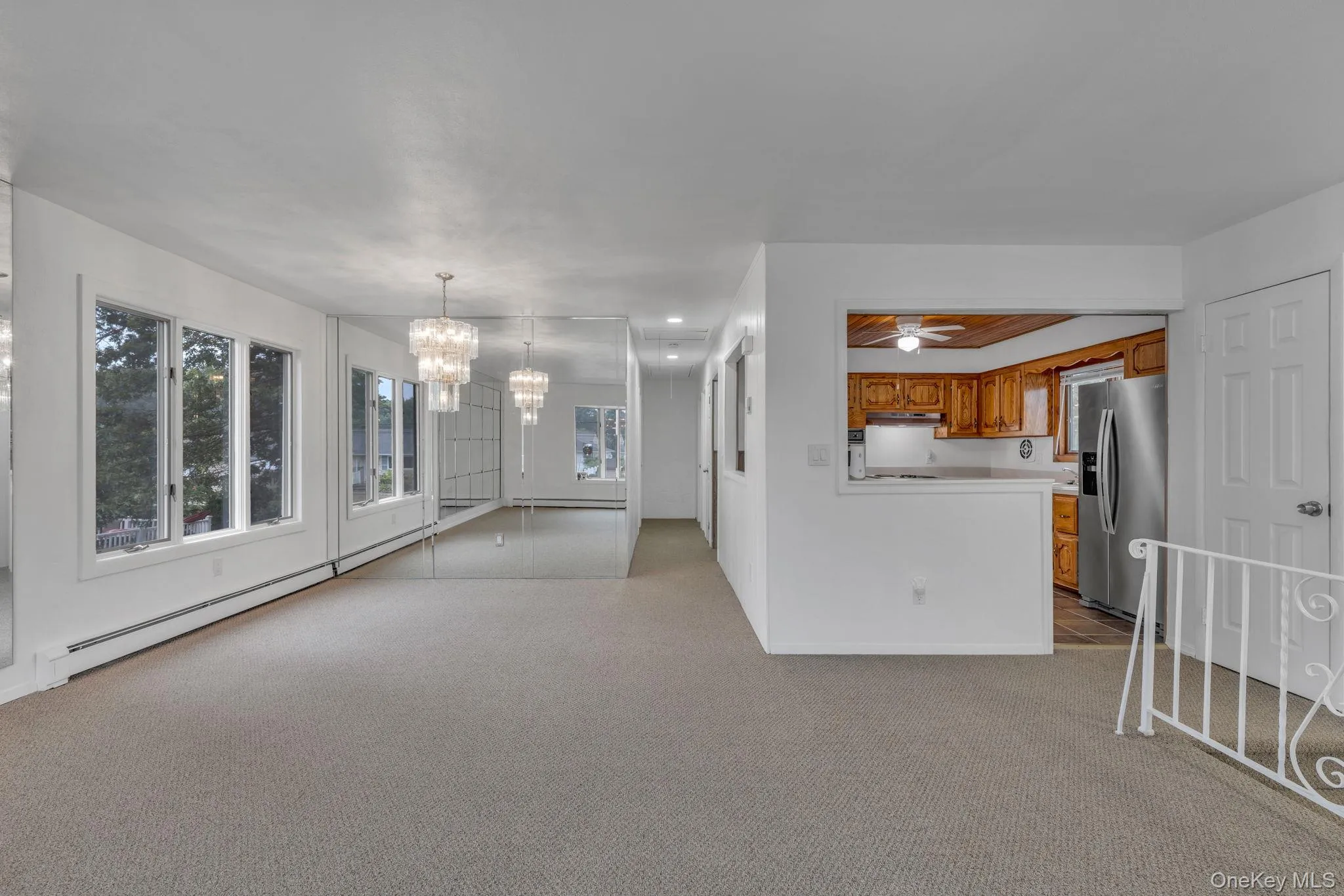 Unfurnished living room featuring a chandelier, light colored carpet, baseboard heating, and ceiling fan Unfurnished living room featuring a chandelier, light colored carpet, baseboard heating, and ceiling fan