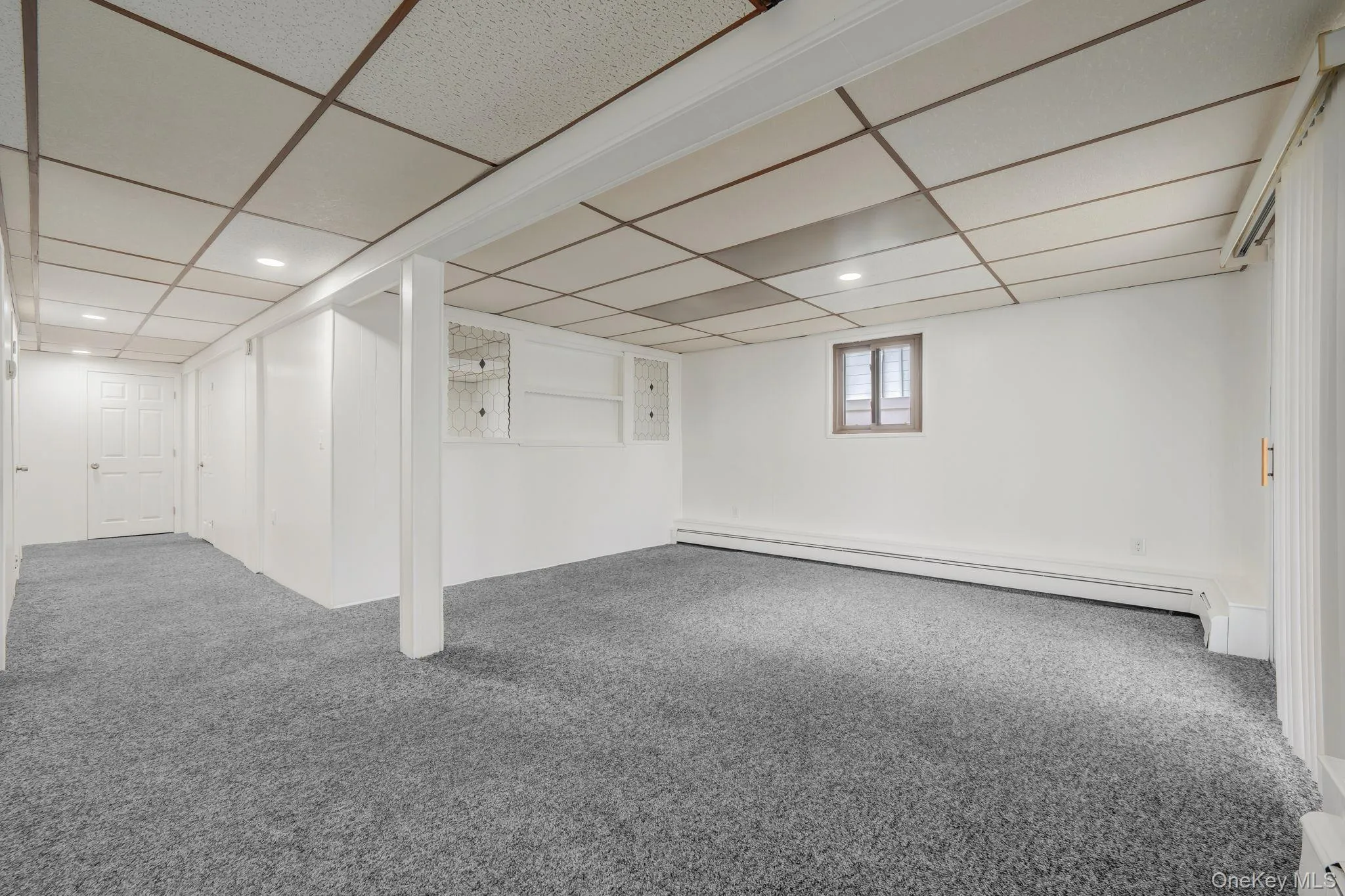 Basement with carpet, a paneled ceiling, a baseboard heating unit, and a baseboard radiator Basement with carpet, a paneled ceiling, a baseboard heating unit, and a baseboard radiator