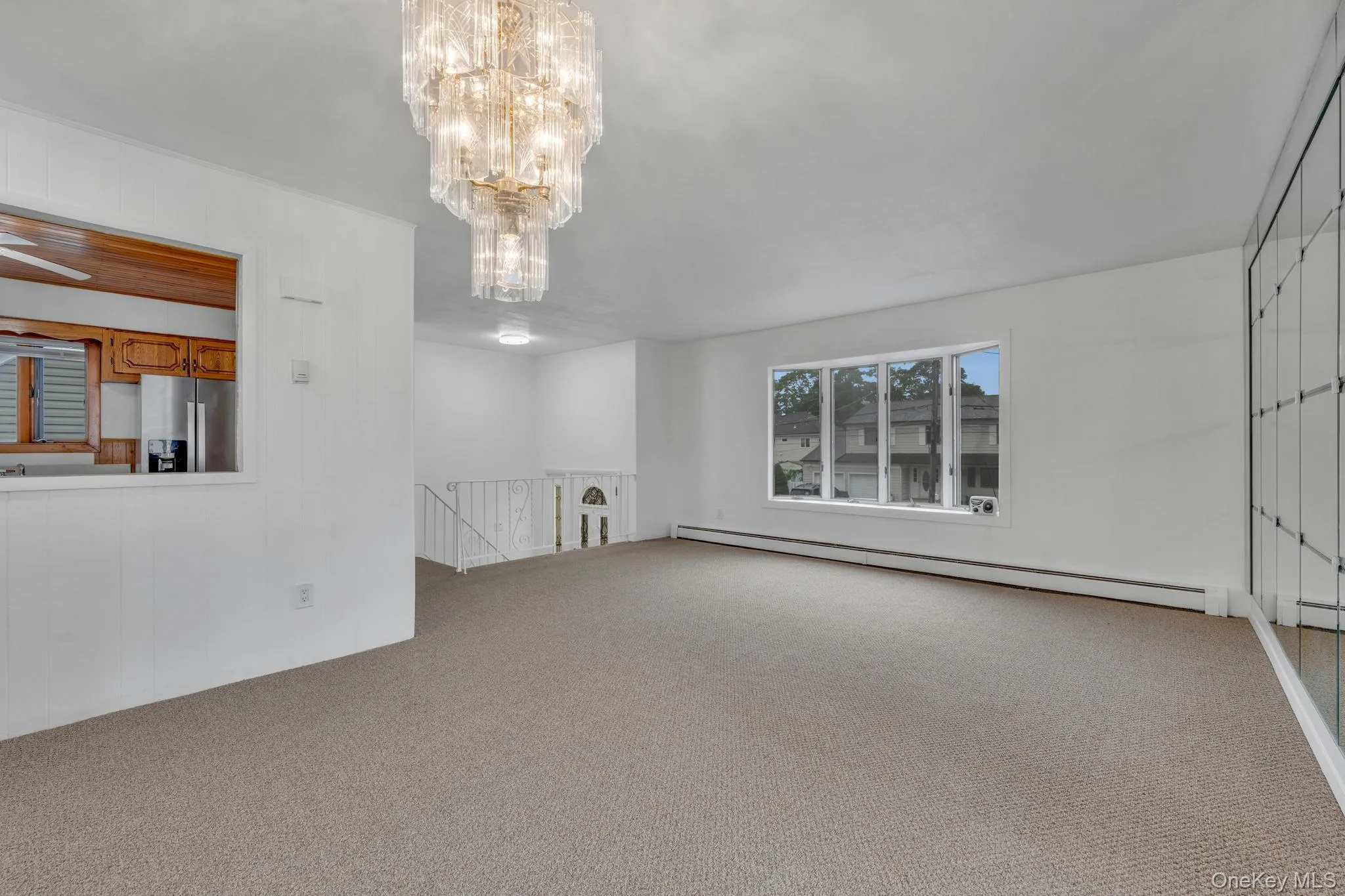 Unfurnished living room with a baseboard heating unit, light colored carpet, and a chandelier Unfurnished living room with a baseboard heating unit, light colored carpet, and a chandelier