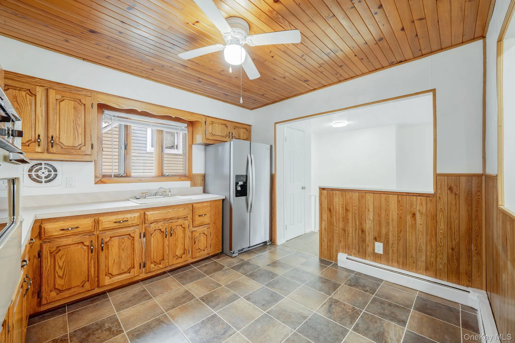 Kitchen with wooden walls, wainscoting, light countertops, stainless steel refrigerator with ice dispenser, and a baseboard heating unit Kitchen with wooden walls, wainscoting, light countertops, stainless steel refrigerator with ice dispenser, and a baseboard heating unit