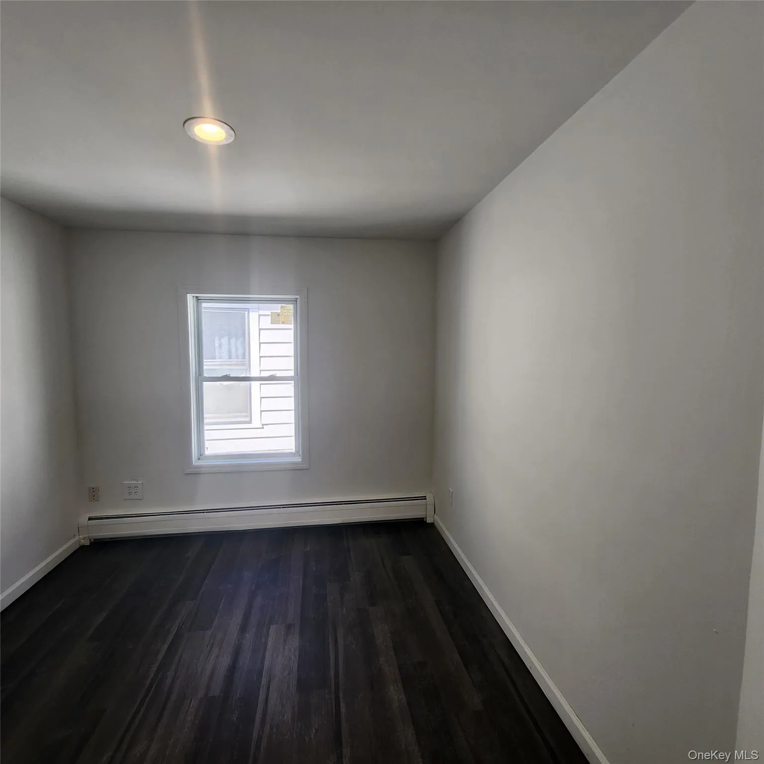 Unfurnished room featuring dark wood finished floors and a baseboard heating unit Unfurnished room featuring dark wood finished floors and a baseboard heating unit