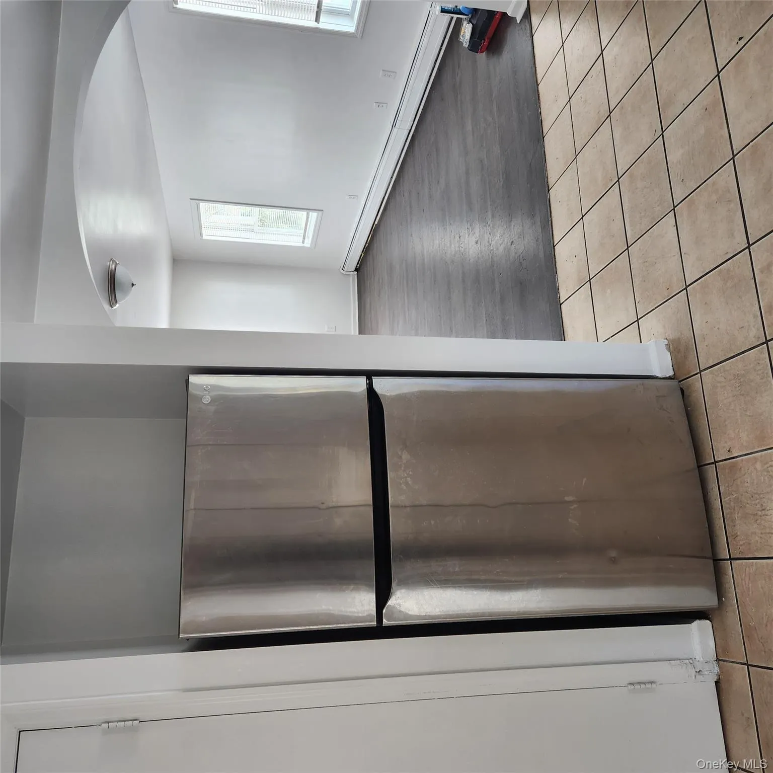 Kitchen featuring stainless steel fridge, light tile patterned flooring, baseboard heating, and arched walkways Kitchen featuring stainless steel fridge, light tile patterned flooring, baseboard heating, and arched walkways
