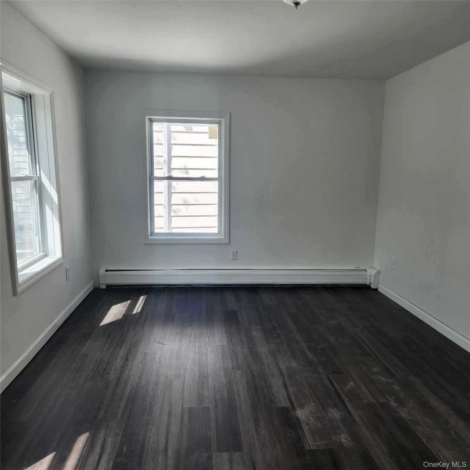 Empty room with dark wood-style floors and baseboard heating Empty room with dark wood-style floors and baseboard heating