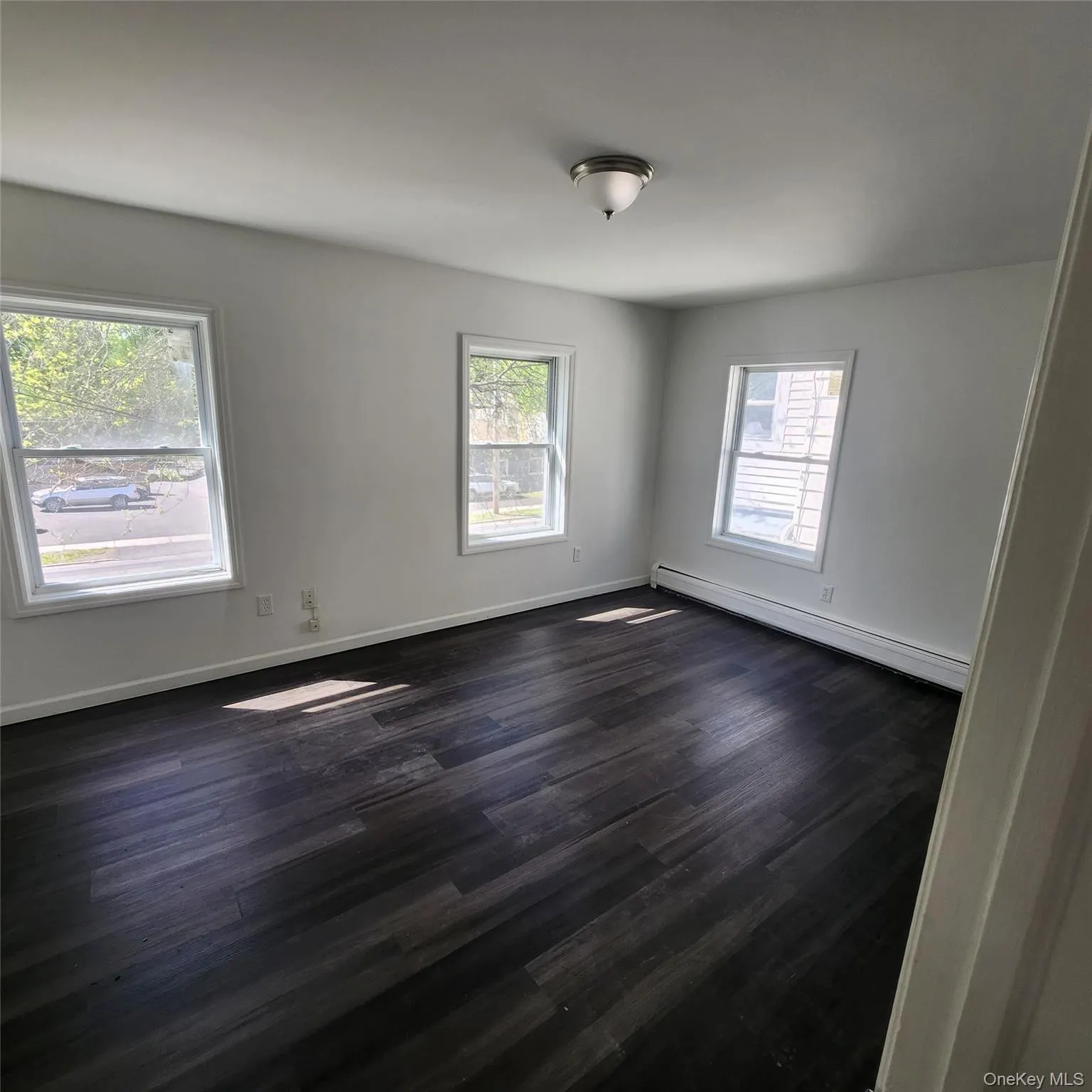 Spare room with a baseboard radiator, plenty of natural light, and dark wood finished floors Spare room with a baseboard radiator, plenty of natural light, and dark wood finished floors