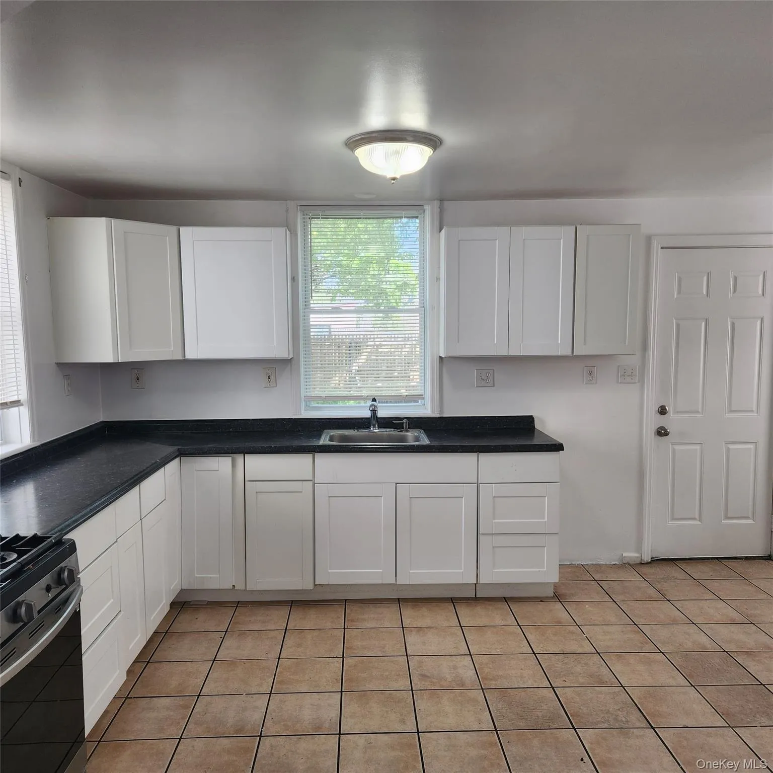 Kitchen featuring white cabinets, light tile patterned flooring, and dark countertops Kitchen featuring white cabinets, light tile patterned flooring, and dark countertops
