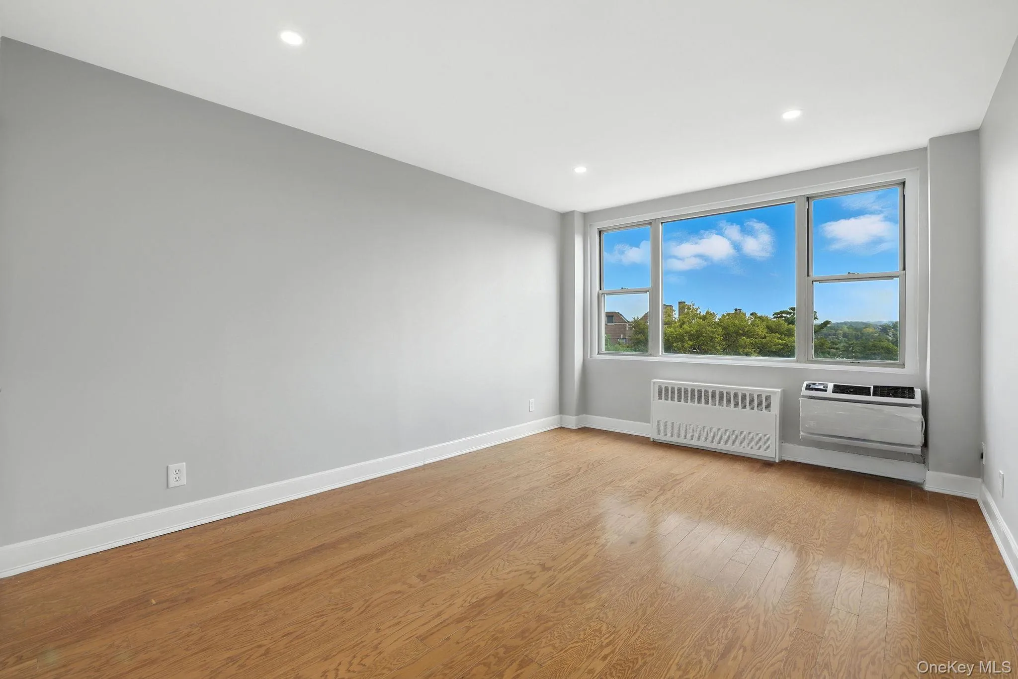 Unfurnished bedroom with radiator heating unit, wood finished floors, recessed lighting, and a wall mounted AC Unfurnished bedroom with radiator heating unit, wood finished floors, recessed lighting, and a wall mounted AC