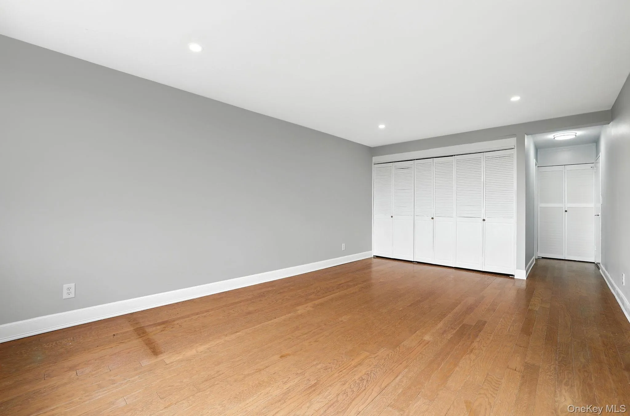 Unfurnished primary bedroom with wood flooring, recessed lighting, and a large closet Unfurnished primary bedroom with wood flooring, recessed lighting, and a large closet