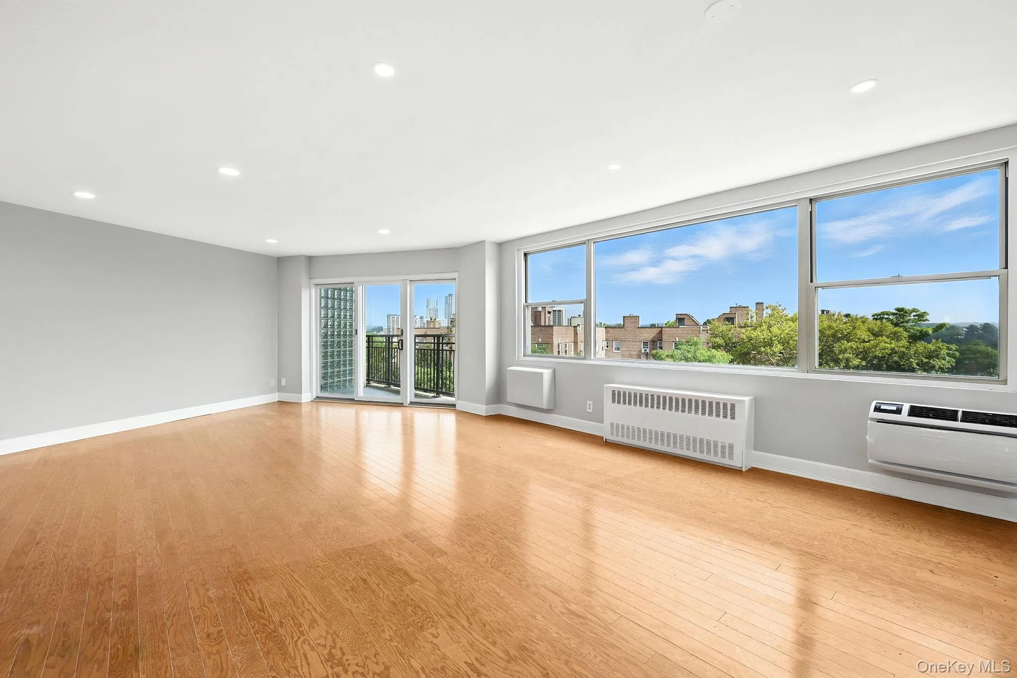 Unfurnished living room with radiator, recessed lighting, light wood flooring, a city view, and a wall mounted air conditioner Unfurnished living room with radiator, recessed lighting, light wood flooring, a city view, and a wall mounted air conditioner