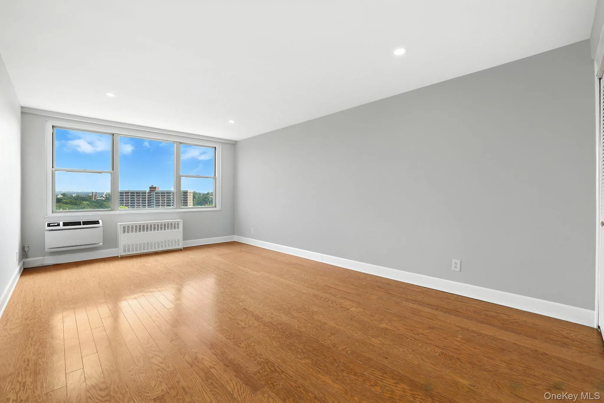 Primary bedroom with radiator, wood flooring, a wall mounted AC, and recessed lighting Primary bedroom with radiator, wood flooring, a wall mounted AC, and recessed lighting