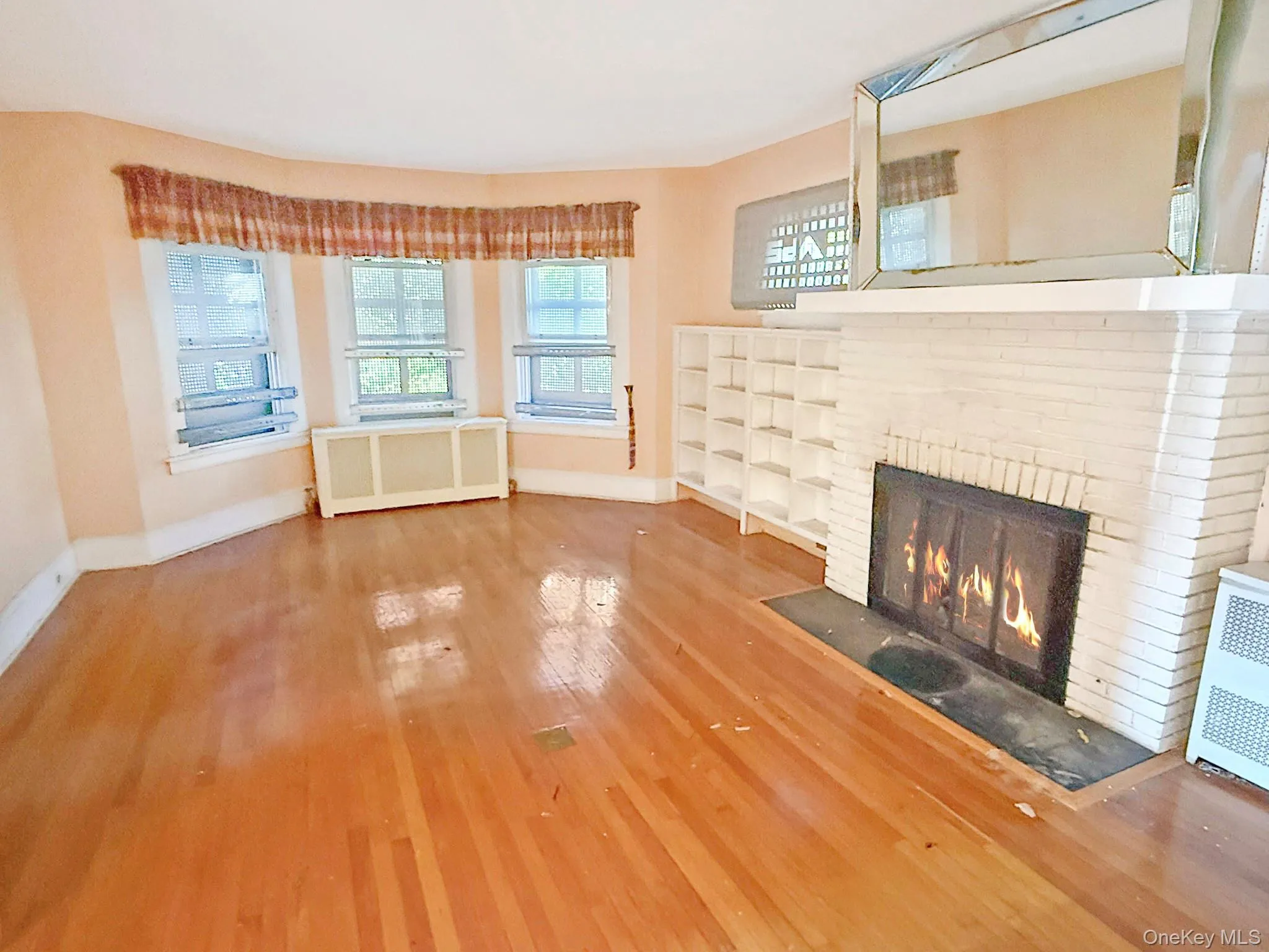 Unfurnished living room with radiator, a brick fireplace, and wood finished floors Unfurnished living room with radiator, a brick fireplace, and wood finished floors