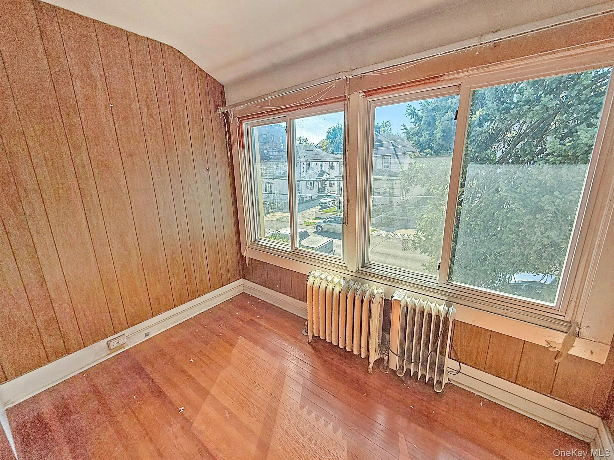 Unfurnished room with wood walls, radiator heating unit, hardwood / wood-style floors, and lofted ceiling Unfurnished room with wood walls, radiator heating unit, hardwood / wood-style floors, and lofted ceiling