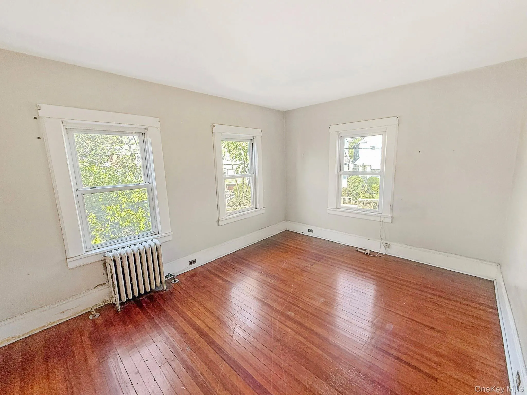 Unfurnished room featuring radiator and hardwood / wood-style floors Unfurnished room featuring radiator and hardwood / wood-style floors