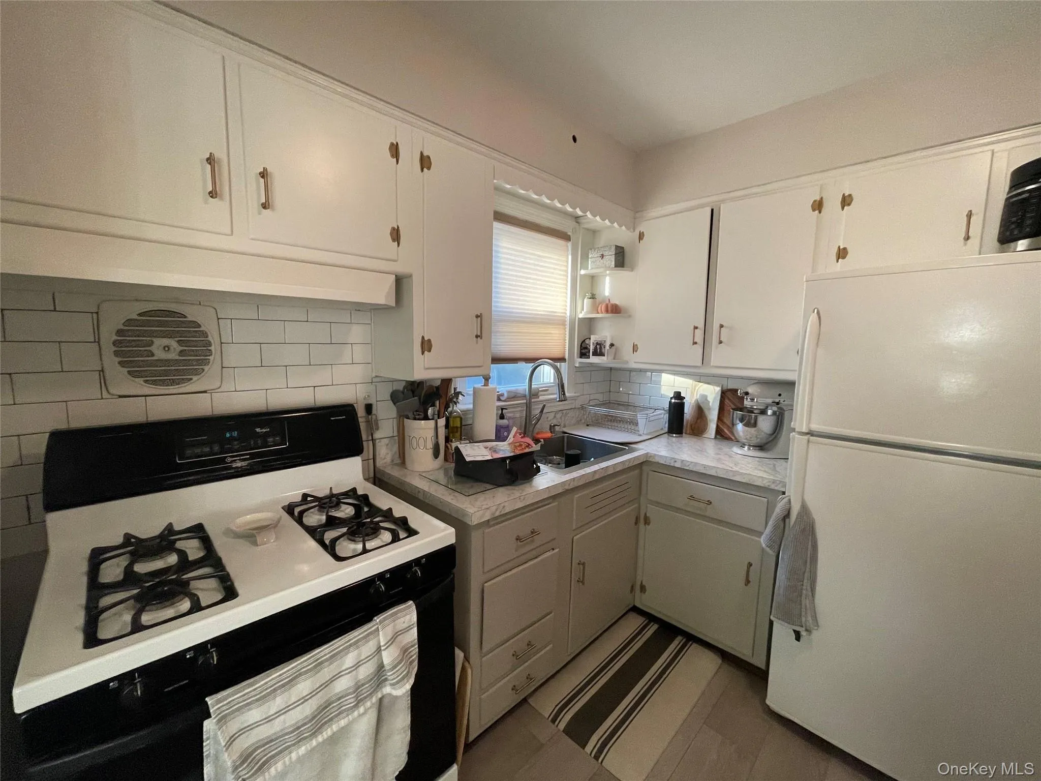 Kitchen with white appliances, light countertops, decorative backsplash, open shelves, and white cabinetry Kitchen with white appliances, light countertops, decorative backsplash, open shelves, and white cabinetry