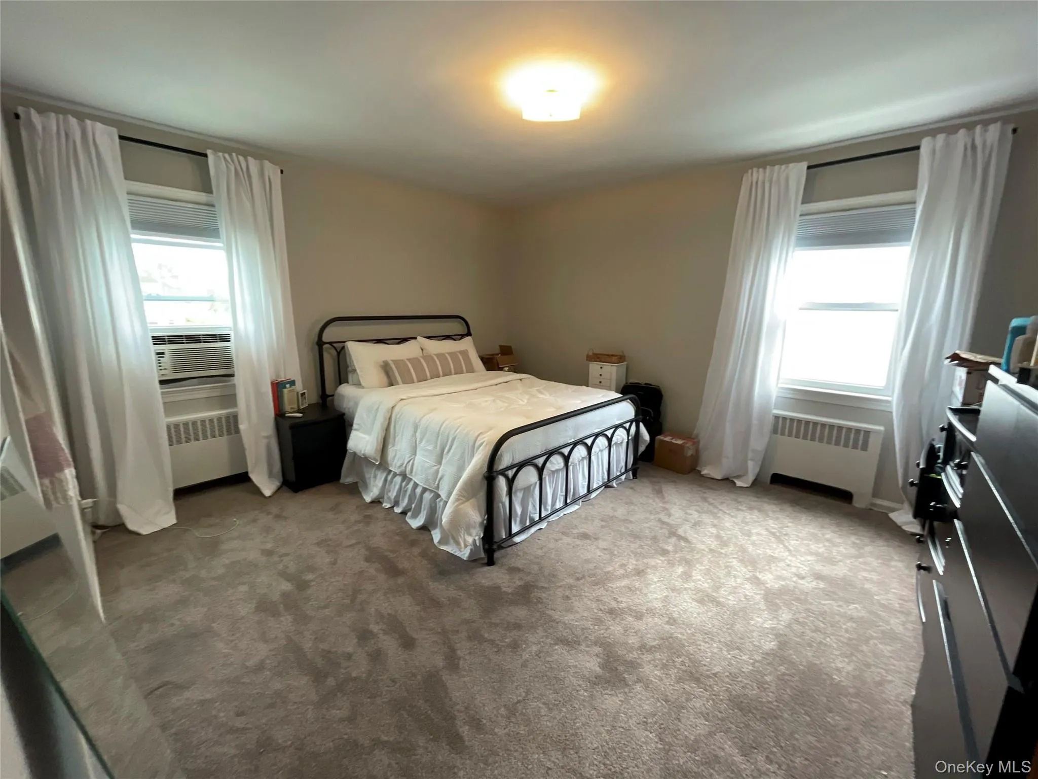 Carpeted bedroom with multiple windows, radiator heating unit, and cooling unit Carpeted bedroom with multiple windows, radiator heating unit, and cooling unit