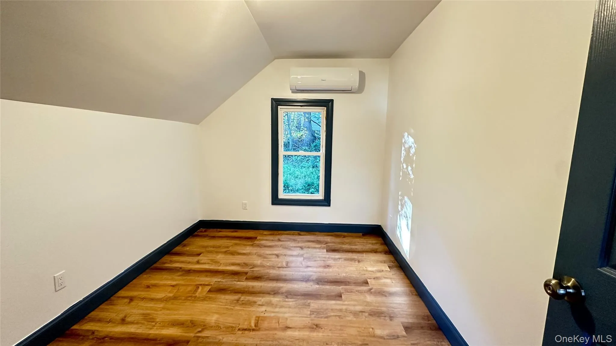 Bedroom with light wood-type flooring, lofted ceiling, and a wall mounted mini-split Bedroom with light wood-type flooring, lofted ceiling, and a wall mounted mini-split