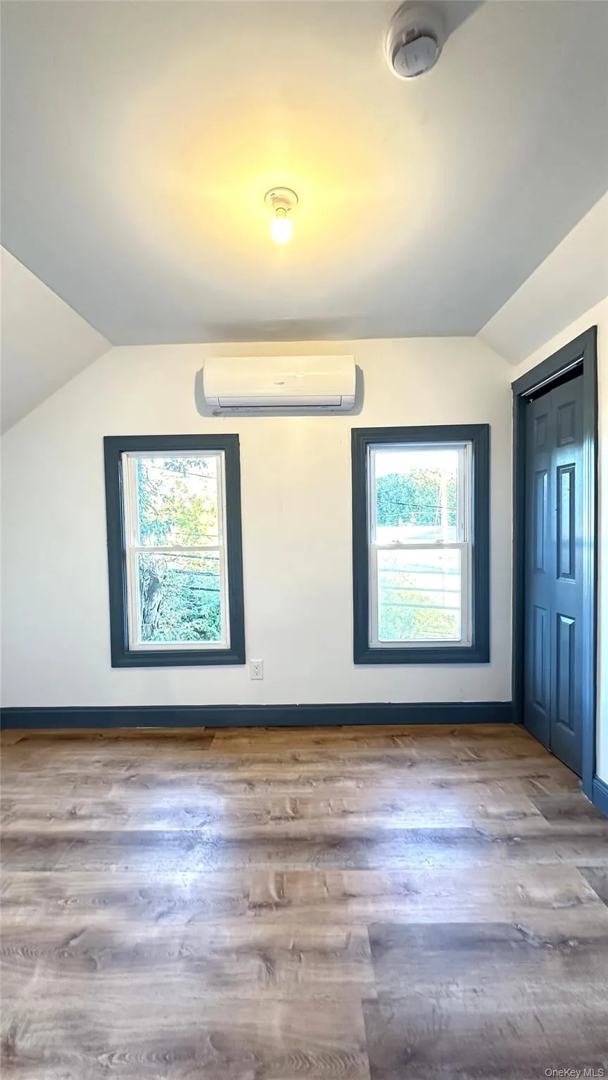 Additional living space featuring vaulted ceiling, wood finished floors, and a wall mounted air conditioner Additional living space featuring vaulted ceiling, wood finished floors, and a wall mounted air conditioner