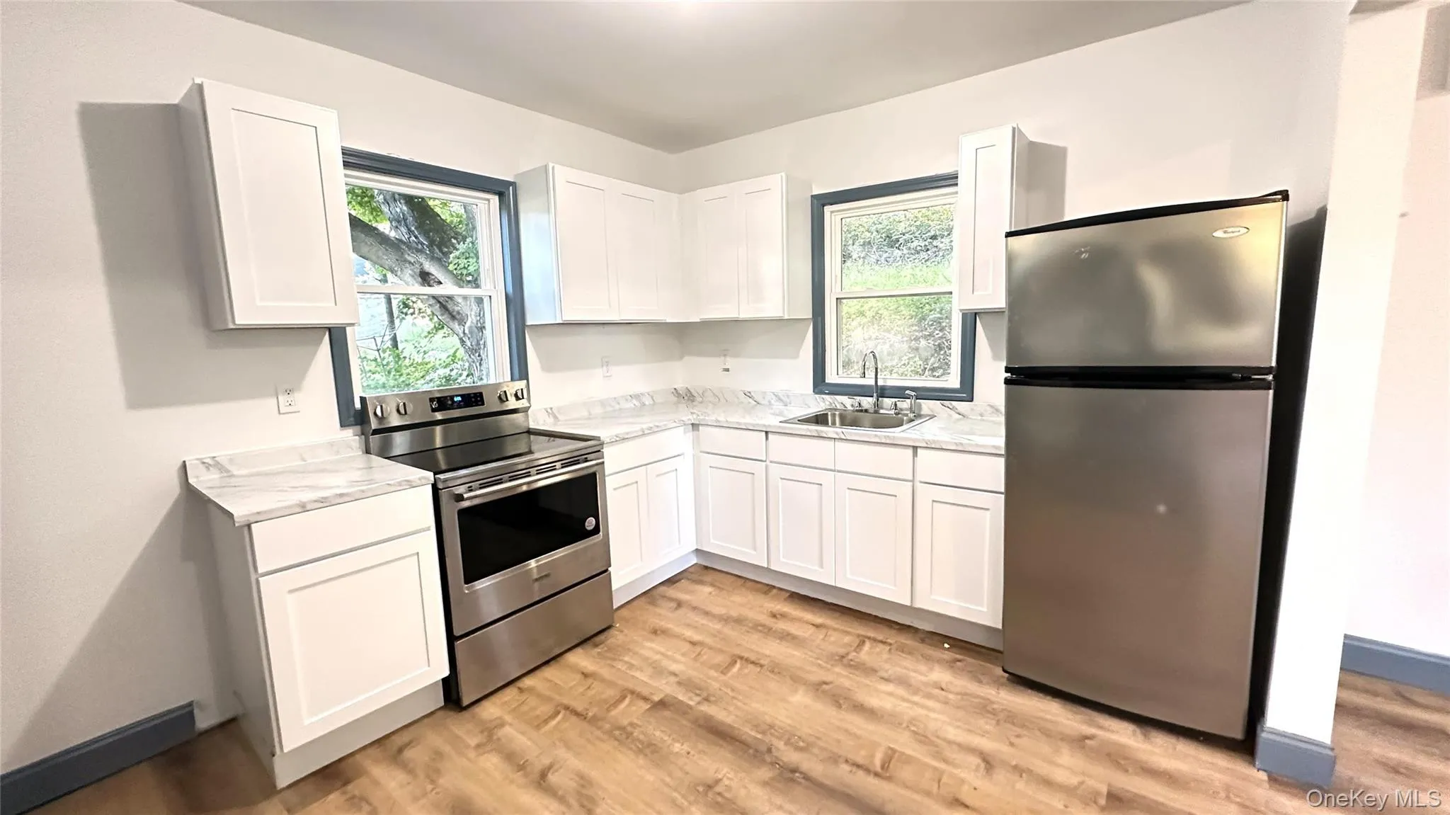 Kitchen featuring stainless steel appliances, white cabinets, light wood-style flooring, and light counters Kitchen featuring stainless steel appliances, white cabinets, light wood-style flooring, and light counters