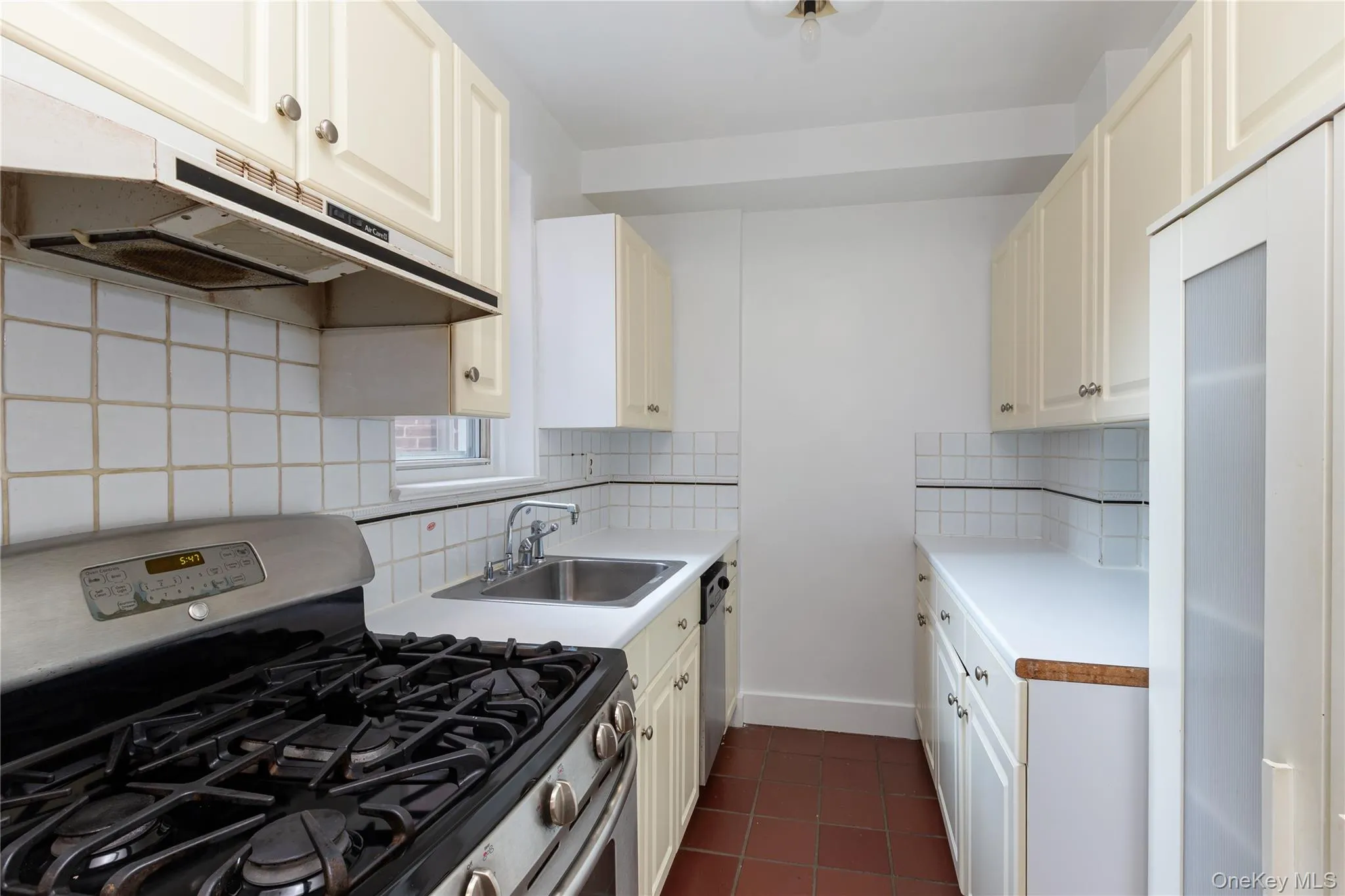 Kitchen featuring stainless steel appliances, tasteful backsplash, dark tile patterned flooring, under cabinet range hood, and light countertops Kitchen featuring stainless steel appliances, tasteful backsplash, dark tile patterned flooring, under cabinet range hood, and light countertops