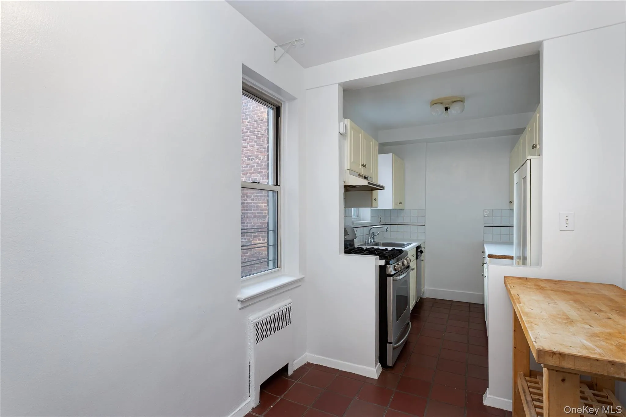 Kitchen with backsplash, radiator, stainless steel gas stove, white cabinets, and dark tile patterned flooring Kitchen with backsplash, radiator, stainless steel gas stove, white cabinets, and dark tile patterned flooring