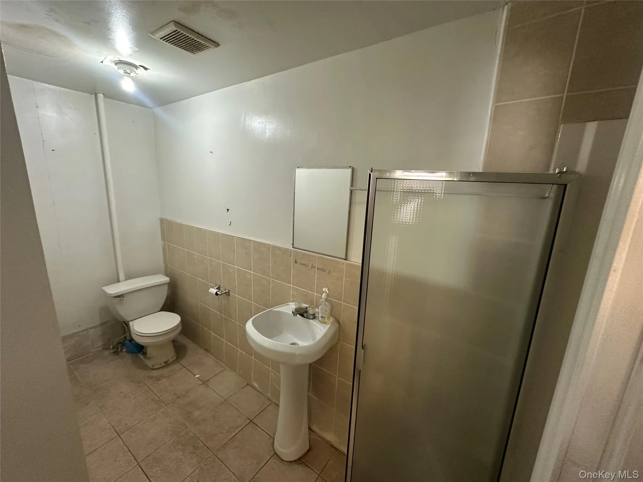 Full bathroom with tile walls, tile patterned flooring, a shower stall, and a wainscoted wall Full bathroom with tile walls, tile patterned flooring, a shower stall, and a wainscoted wall