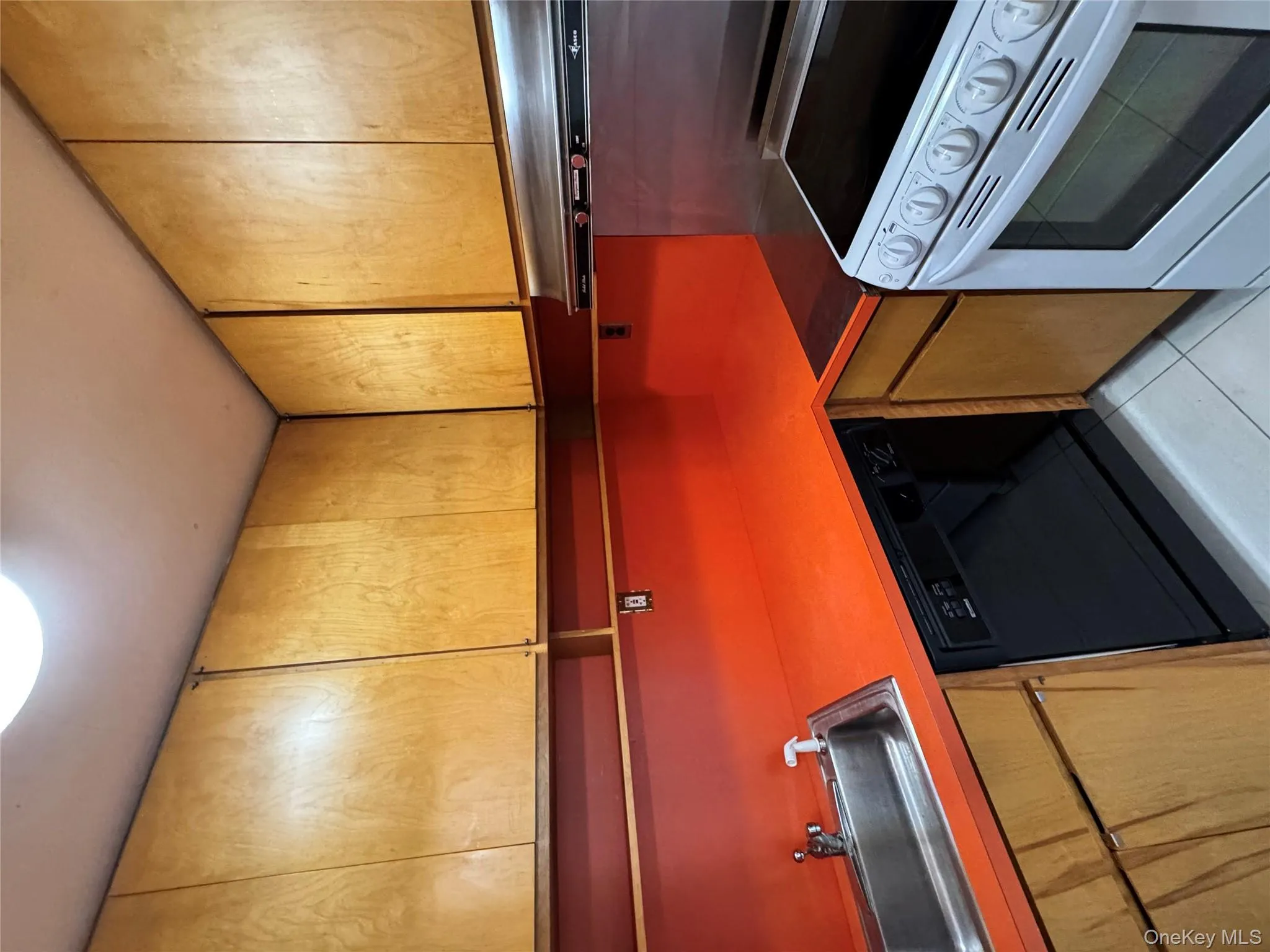Kitchen featuring stove, dishwasher, range hood, light tile patterned floors, and brown cabinetry Kitchen featuring stove, dishwasher, range hood, light tile patterned floors, and brown cabinetry