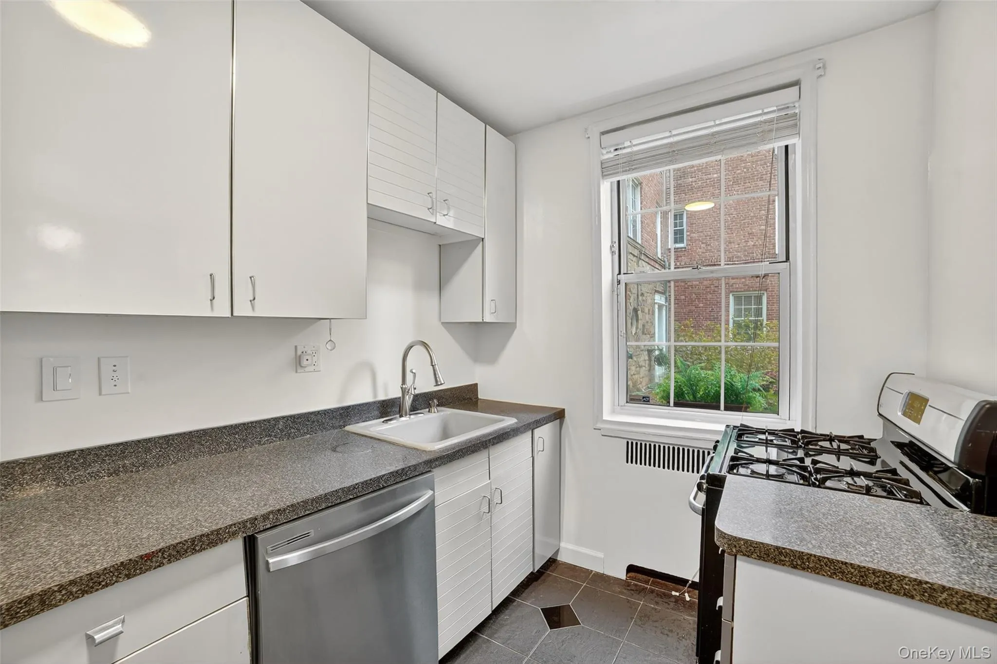 Kitchen featuring stainless steel appliances, dark countertops, dark tile patterned floors, and white cabinetry Kitchen featuring stainless steel appliances, dark countertops, dark tile patterned floors, and white cabinetry