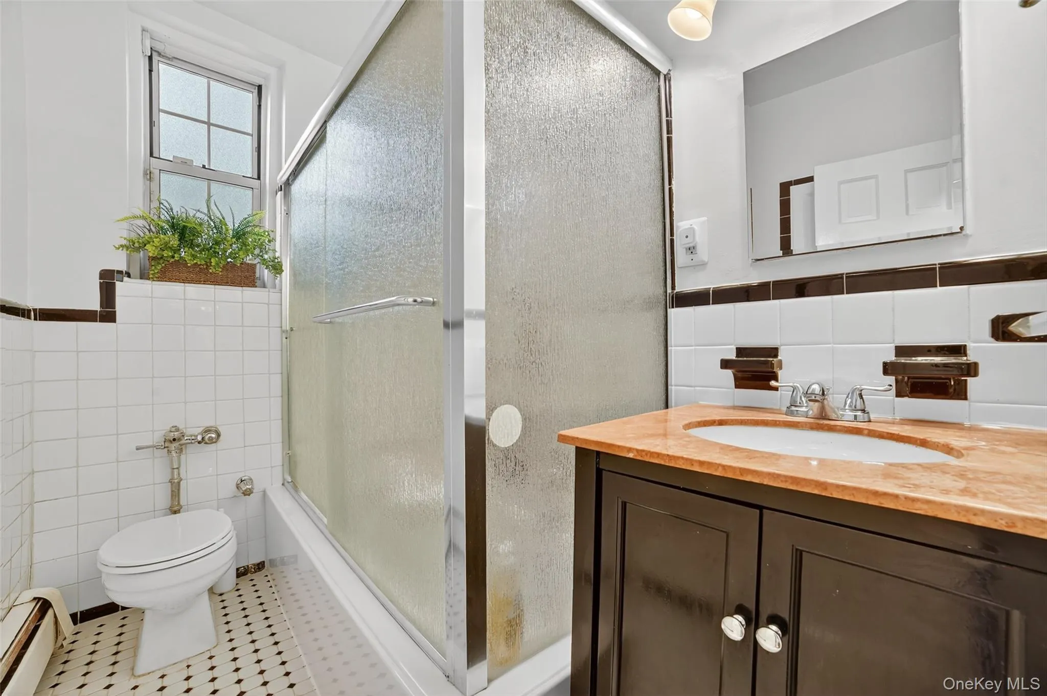 Bathroom with tile walls, vanity, a baseboard heating unit, combined bath / shower with glass door, and a wainscoted wall Bathroom with tile walls, vanity, a baseboard heating unit, combined bath / shower with glass door, and a wainscoted wall