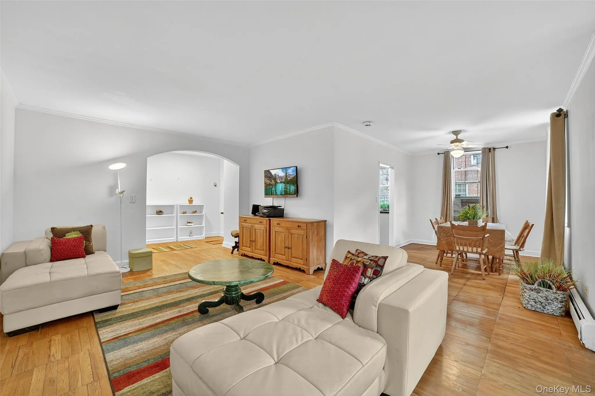 Living room with crown molding, arched walkways, ceiling fan, light wood finished floors, and a baseboard radiator Living room with crown molding, arched walkways, ceiling fan, light wood finished floors, and a baseboard radiator