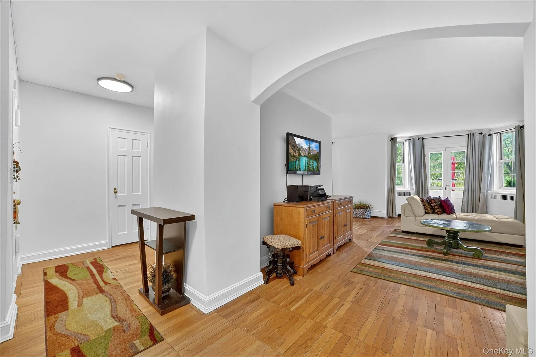 Living area with arched walkways, light wood-type flooring, and crown molding Living area with arched walkways, light wood-type flooring, and crown molding