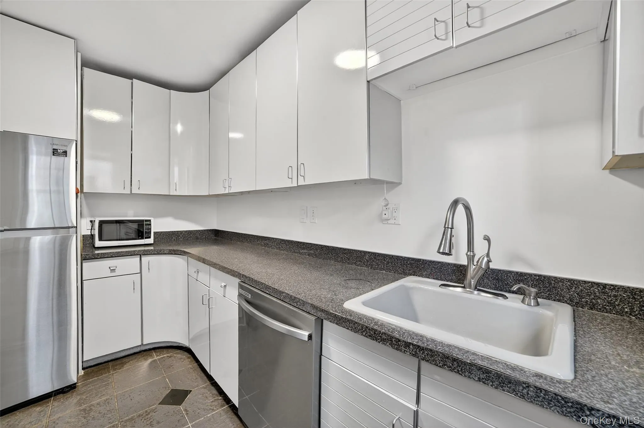 Kitchen with appliances with stainless steel finishes, white cabinets, dark countertops, and dark stone finish floors Kitchen with appliances with stainless steel finishes, white cabinets, dark countertops, and dark stone finish floors