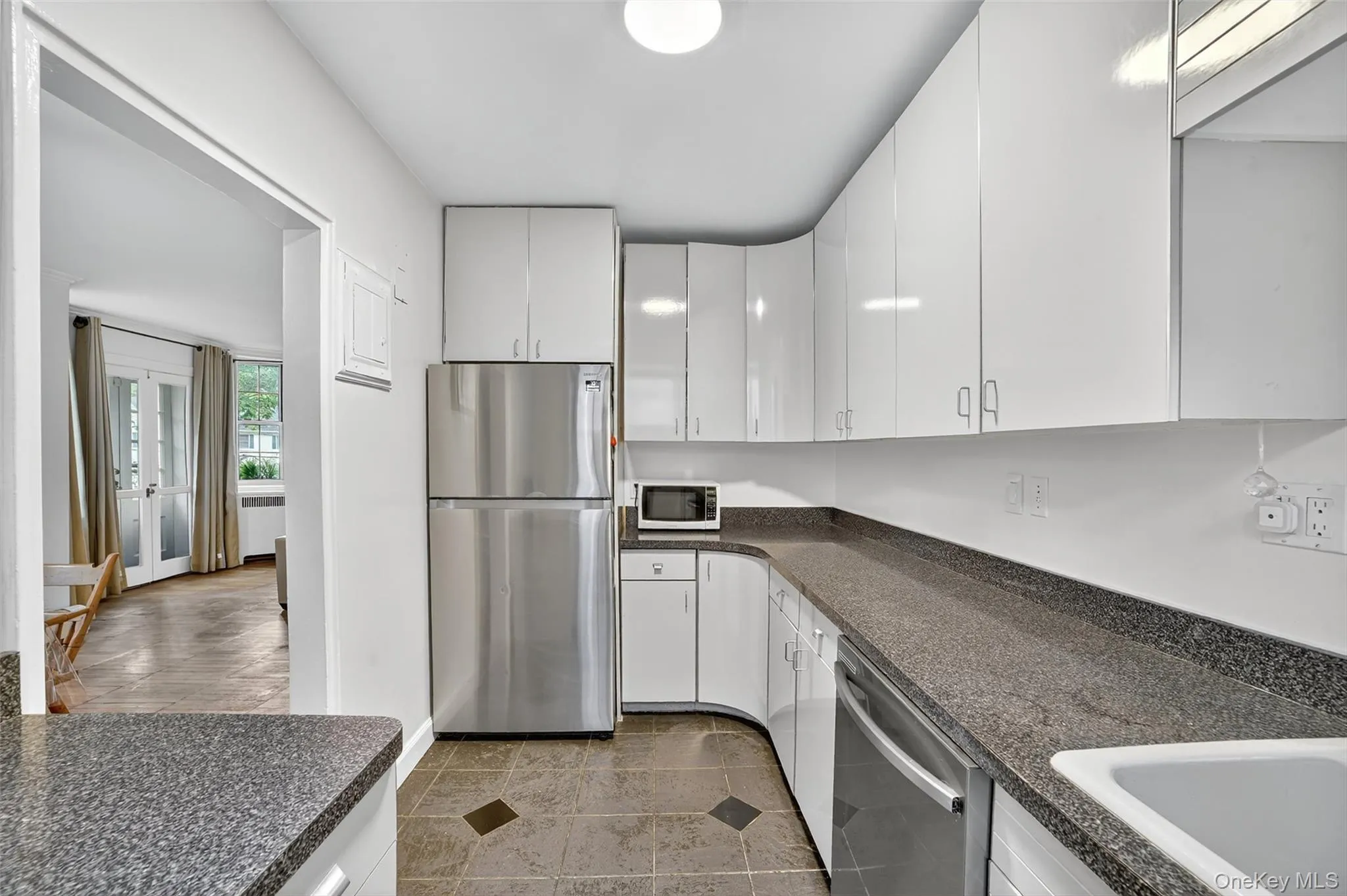 Kitchen with appliances with stainless steel finishes, white cabinets, dark tile patterned floors, radiator, and dark stone counters Kitchen with appliances with stainless steel finishes, white cabinets, dark tile patterned floors, radiator, and dark stone counters