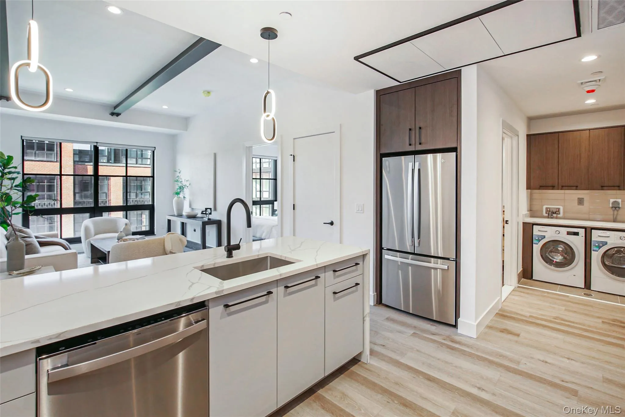 Kitchen featuring stainless steel appliances, white cabinetry, washing machine and clothes dryer, and decorative light fixtures Kitchen featuring stainless steel appliances, white cabinetry, washing machine and clothes dryer, and decorative light fixtures