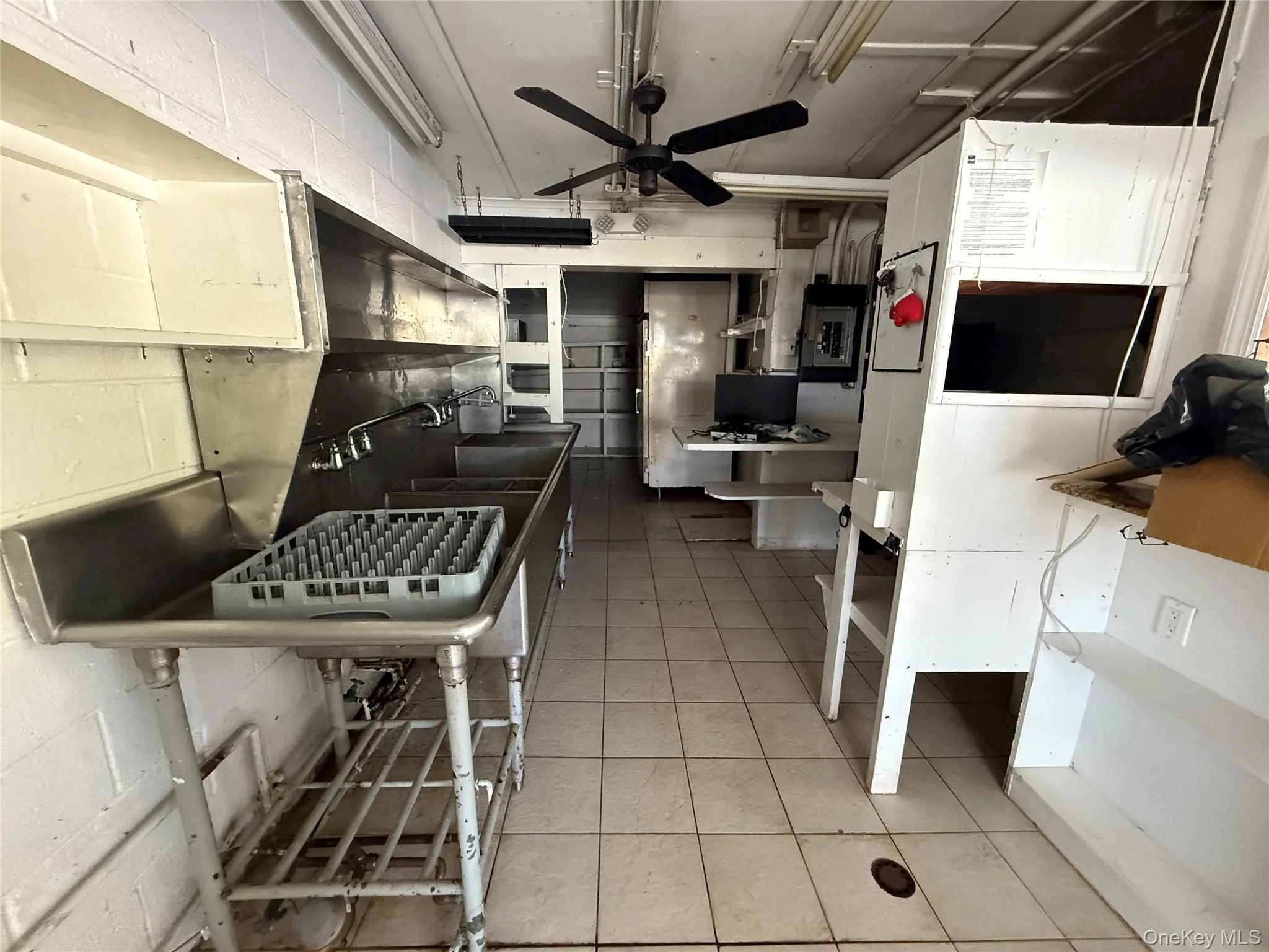 Kitchen with a ceiling fan, light tile patterned floors, electric panel, and concrete block wall Kitchen with a ceiling fan, light tile patterned floors, electric panel, and concrete block wall