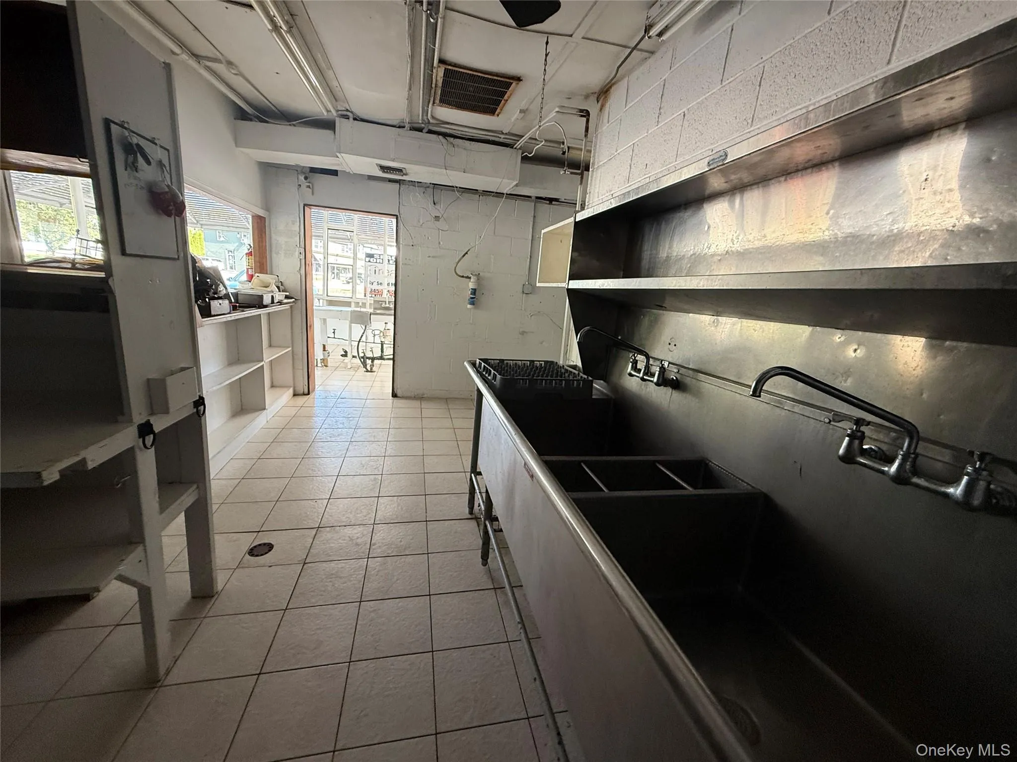 Kitchen with open shelves, light tile patterned floors, and concrete block wall Kitchen with open shelves, light tile patterned floors, and concrete block wall