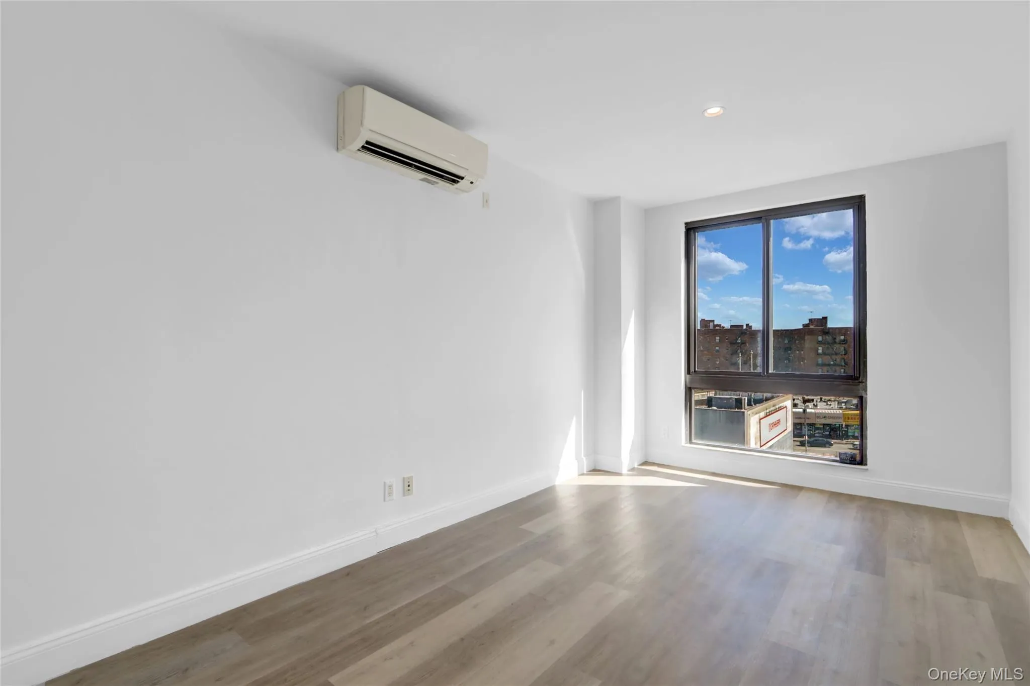 Empty room with a wall mounted AC, wood finished floors, recessed lighting, and a city view Empty room with a wall mounted AC, wood finished floors, recessed lighting, and a city view