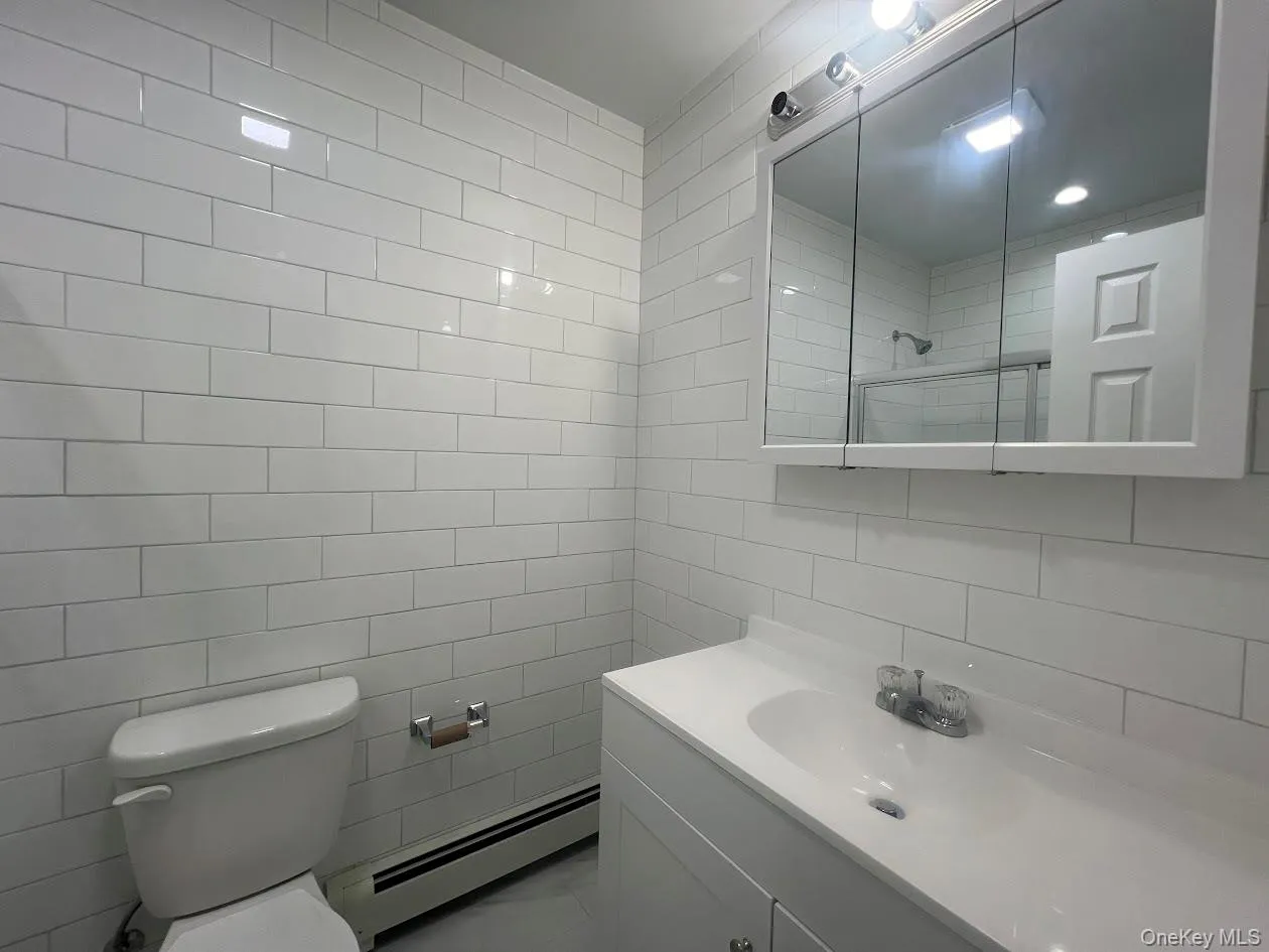 Bathroom featuring a baseboard radiator, tile walls, vanity, tiled shower, and tasteful backsplash Bathroom featuring a baseboard radiator, tile walls, vanity, tiled shower, and tasteful backsplash