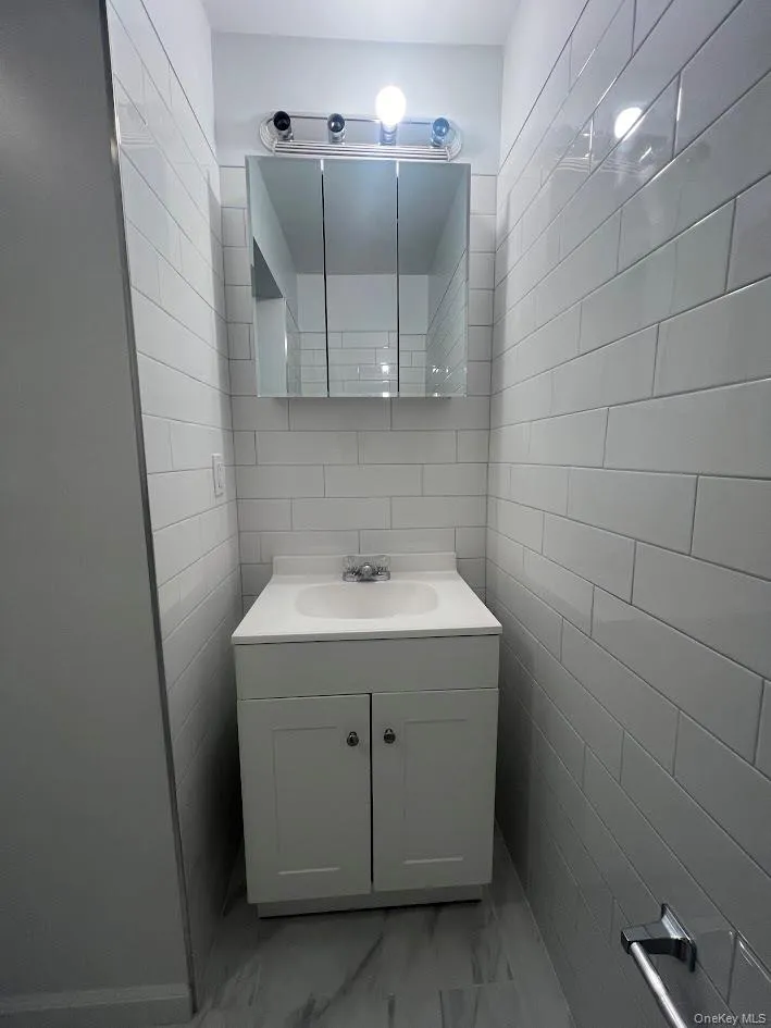 Bathroom featuring vanity, tile walls, and light marble finish floors Bathroom featuring vanity, tile walls, and light marble finish floors